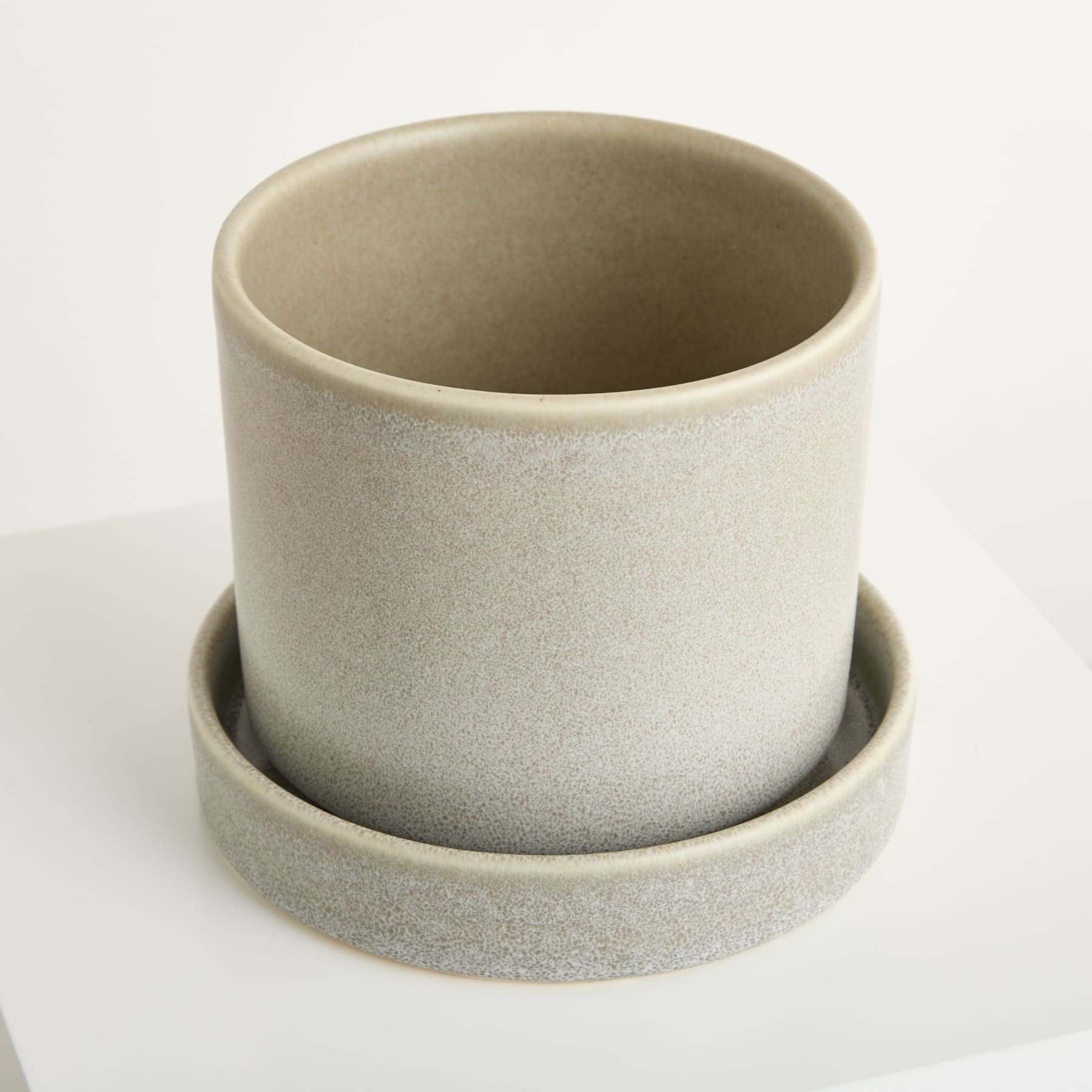 Ein einfacher, minimalistischer Blumentopf oder Topf aus Keramik in einem gedämpften Erdton steht auf einer schlichten weißen Oberfläche.
