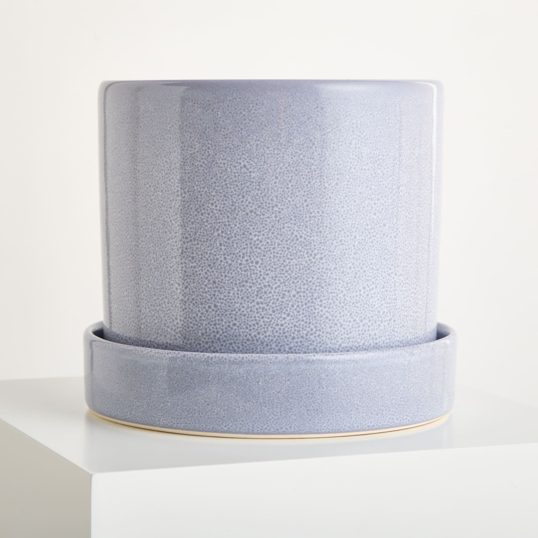 Ein grauer Keramik-Pflanztopf mit Untertasse steht auf einer weißen Oberfläche. Seine matte Oberfläche und das schlichte Design sorgen für ein minimalistisches und elegantes Erscheinungsbild.