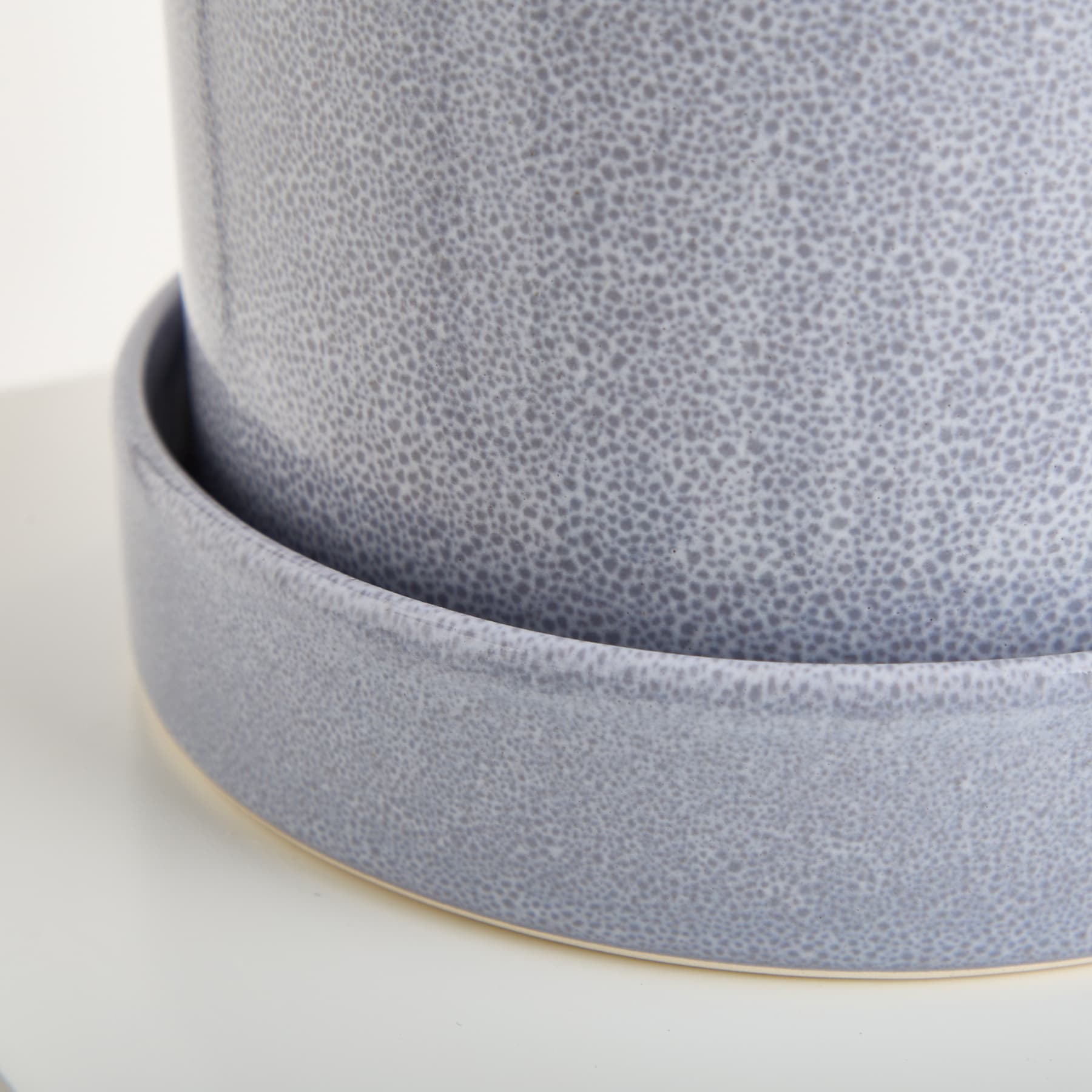 Das Bild zeigt eine Nahaufnahme eines grauen, strukturierten Keramik- oder Porzellanbehälters mit abgerundeter Form und leicht erhöhtem Boden.