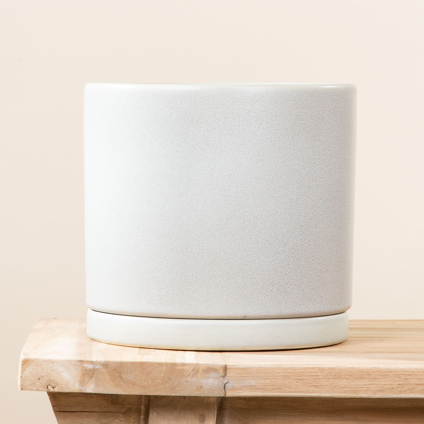 Ein weißer Blumentopf oder Topf aus Keramik steht auf einer Holzoberfläche mit einem schlichten, hellen Hintergrund.