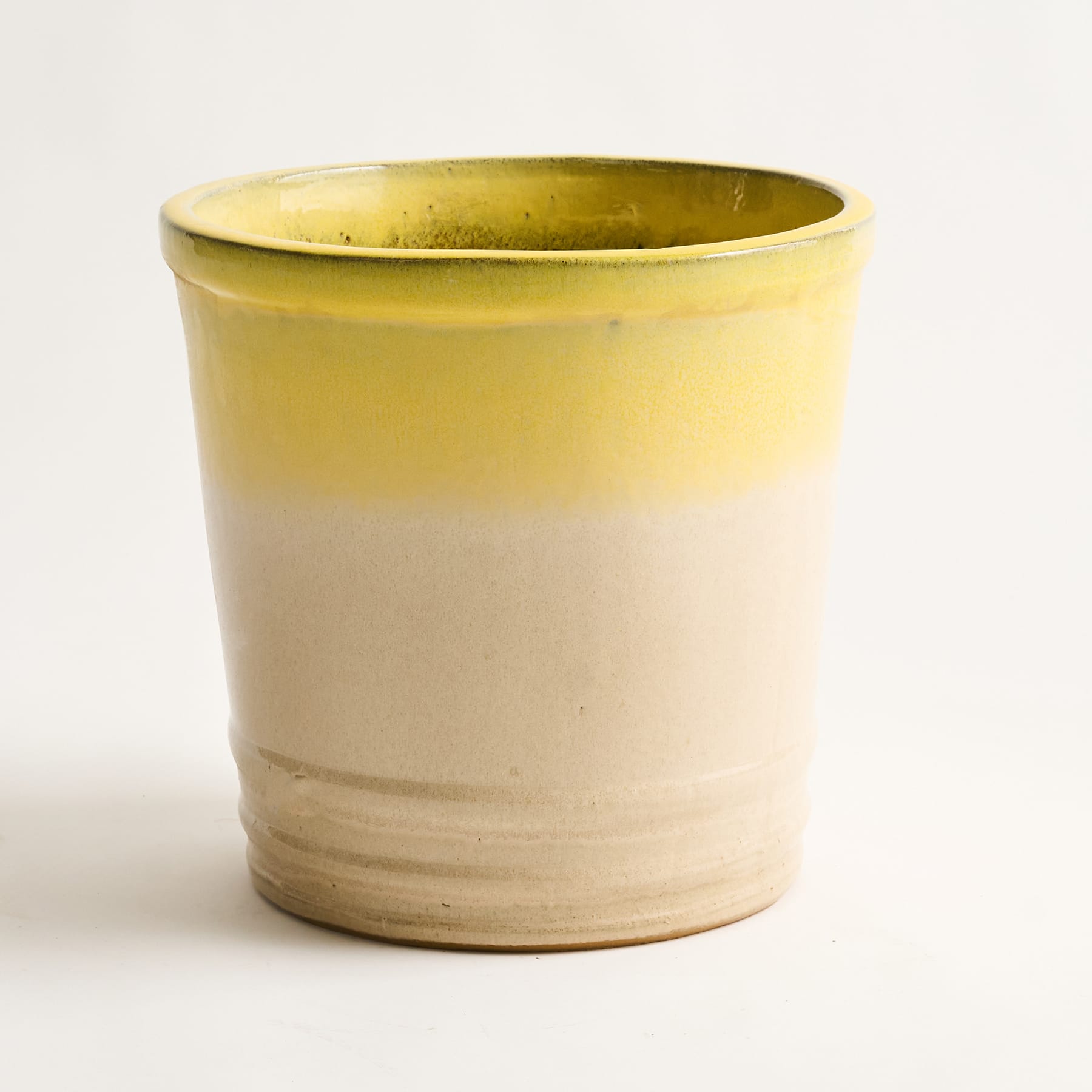 Auf einem schlichten Hintergrund steht eine gelb-weiße Keramiktasse oder ein Becher mit glatter, glänzender Oberfläche und schlichtem, minimalistischem Design.