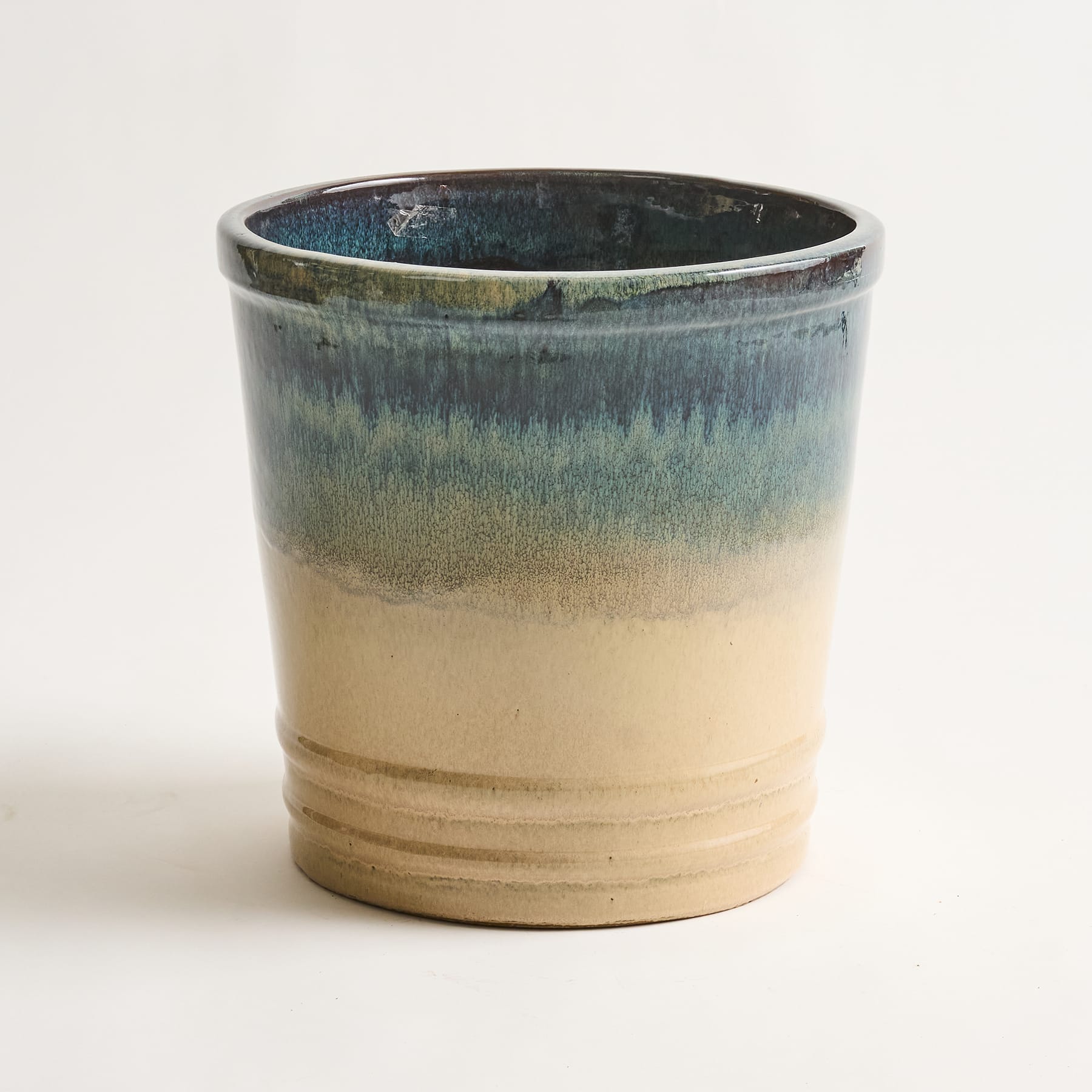 Eine Tasse oder ein Behälter aus Keramik mit einer glasierten Oberfläche in Blau-, Grün- und Beigetönen, die ein strukturiertes und vielschichtiges Erscheinungsbild aufweist.