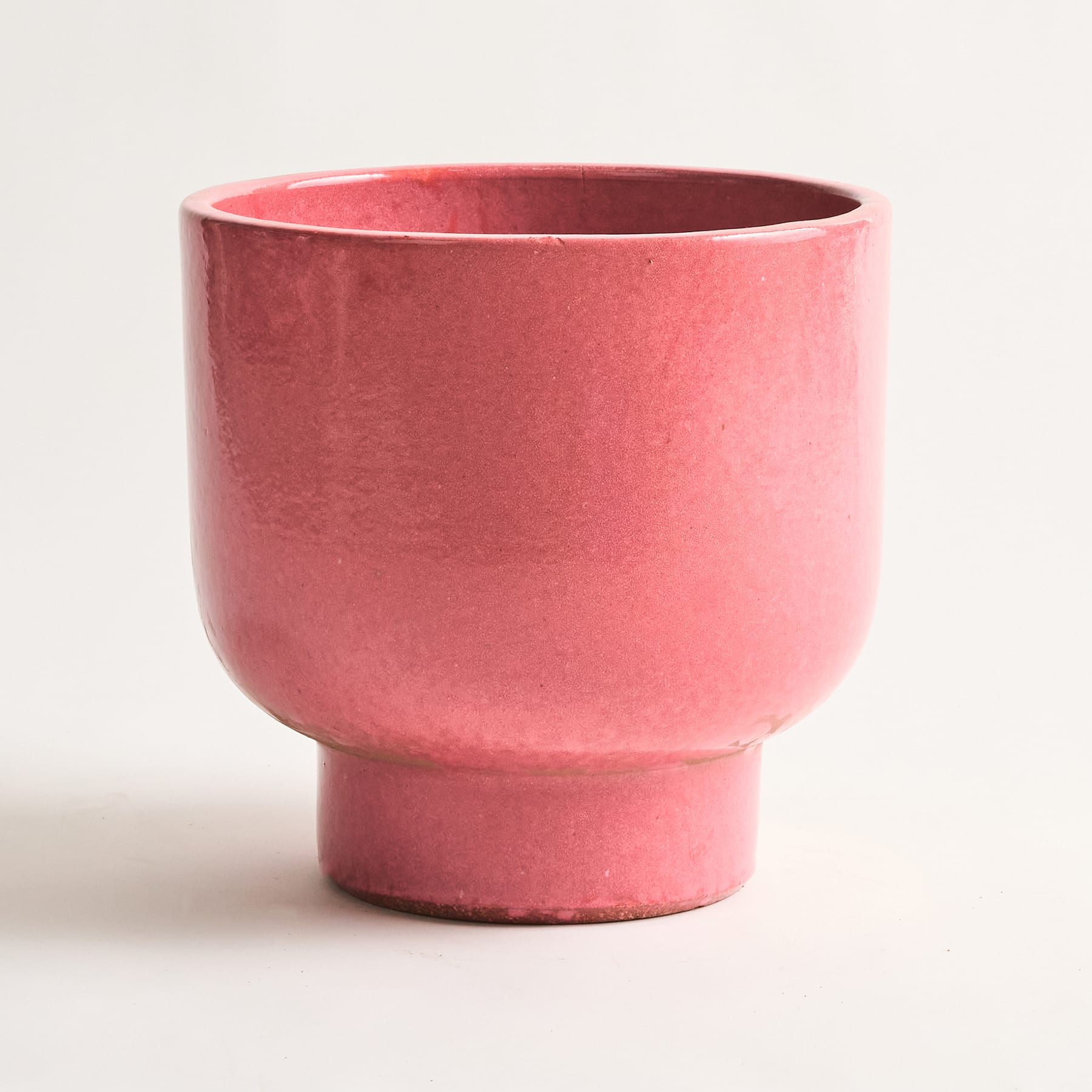 Auf einem schlichten weißen Hintergrund steht ein leuchtend rosa Keramikgefäß mit einer abgerundeten, schalenartigen Form.