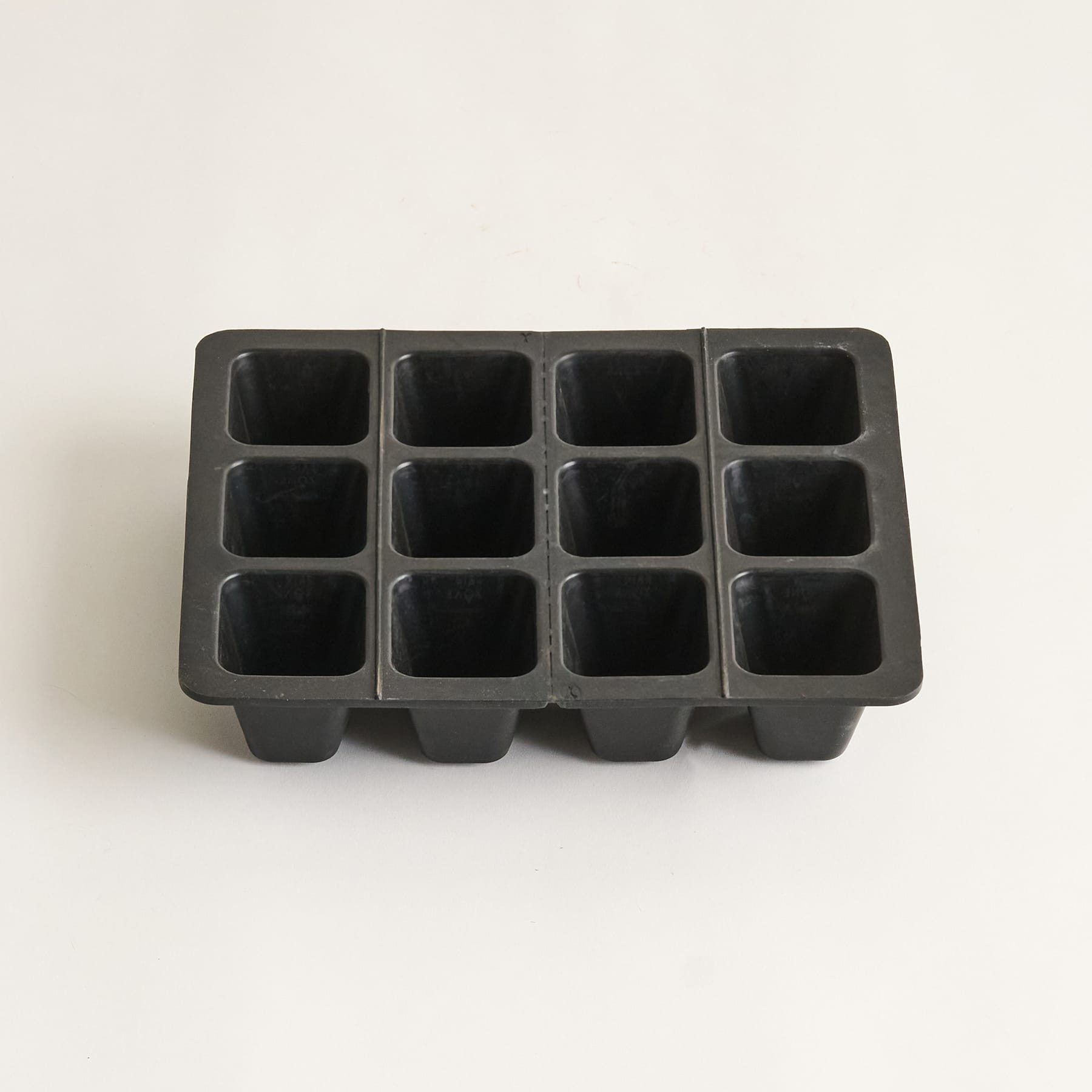 Eine schwarze Plastikschale mit mehreren Fächern, die mit Erde gefüllt sind und aus deren Erde kleine grüne Sprossen sprießen.