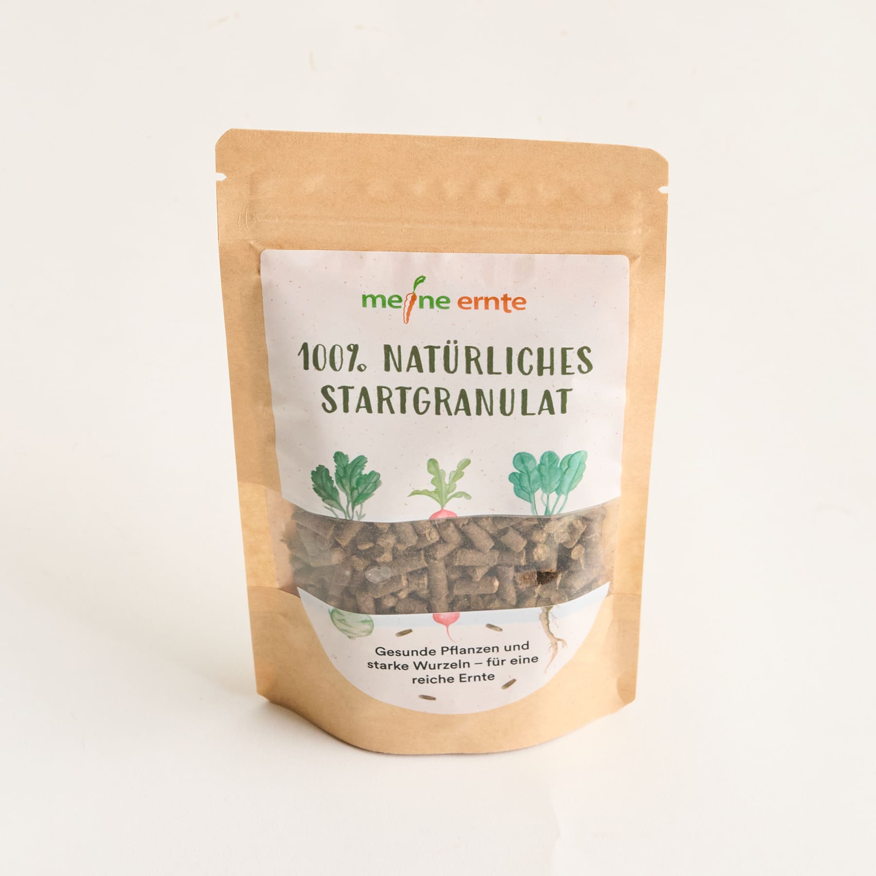 Das Bild zeigt eine gelbe Papiertüte, die eine Packung 100 % natürliches Startergranulat enthält. Auf der Verpackung sind Abbildungen verschiedener grüner Gemüsesorten zu sehen.