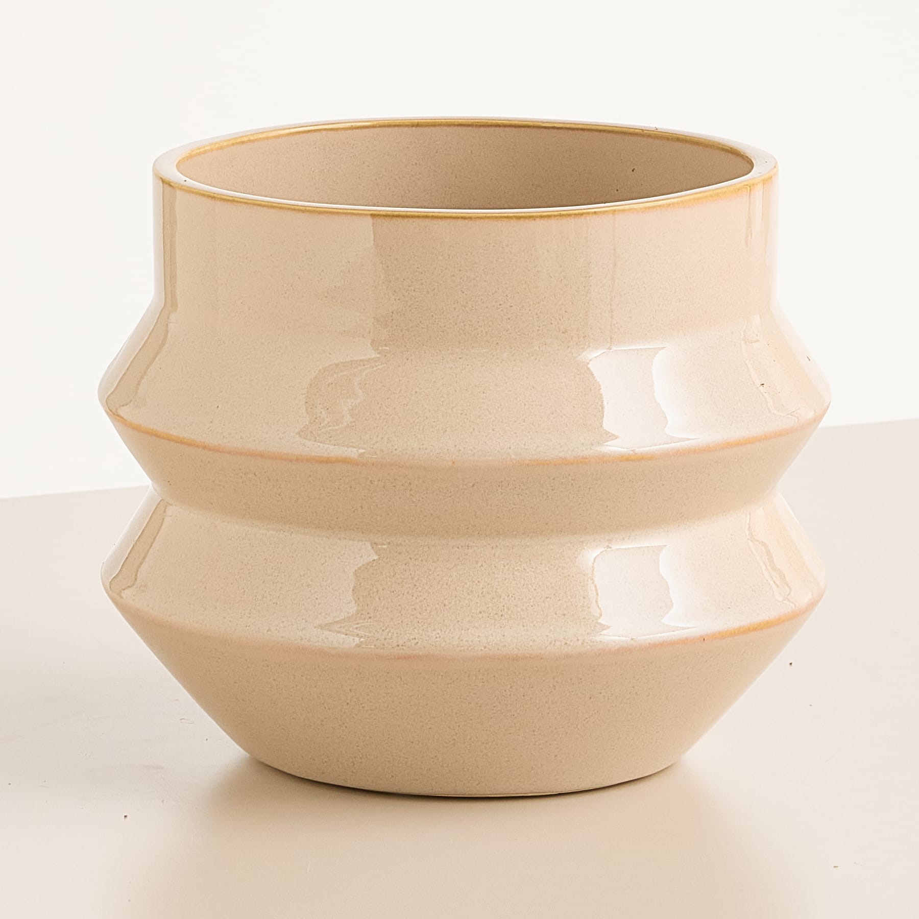 Eine beige Keramikschale mit abgerundetem Stufendesign steht auf einem schlichten weißen Hintergrund.