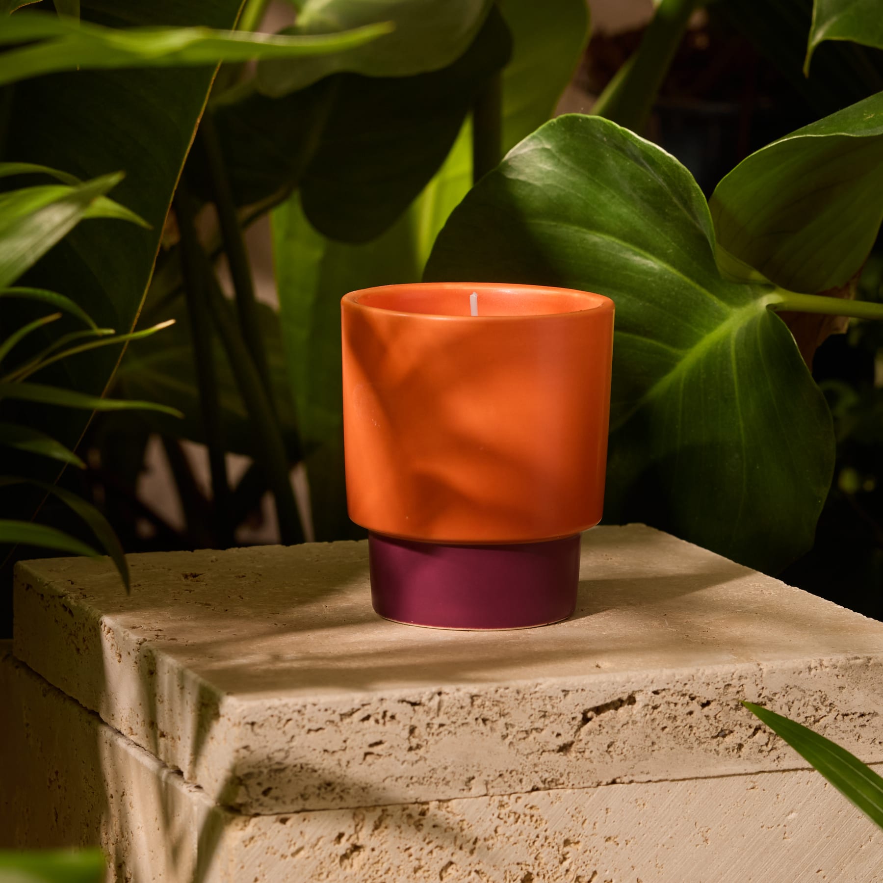 Ein leuchtend orangefarbener Kerzenhalter mit violettem Sockel steht auf einem schlichten weißen Hintergrund.