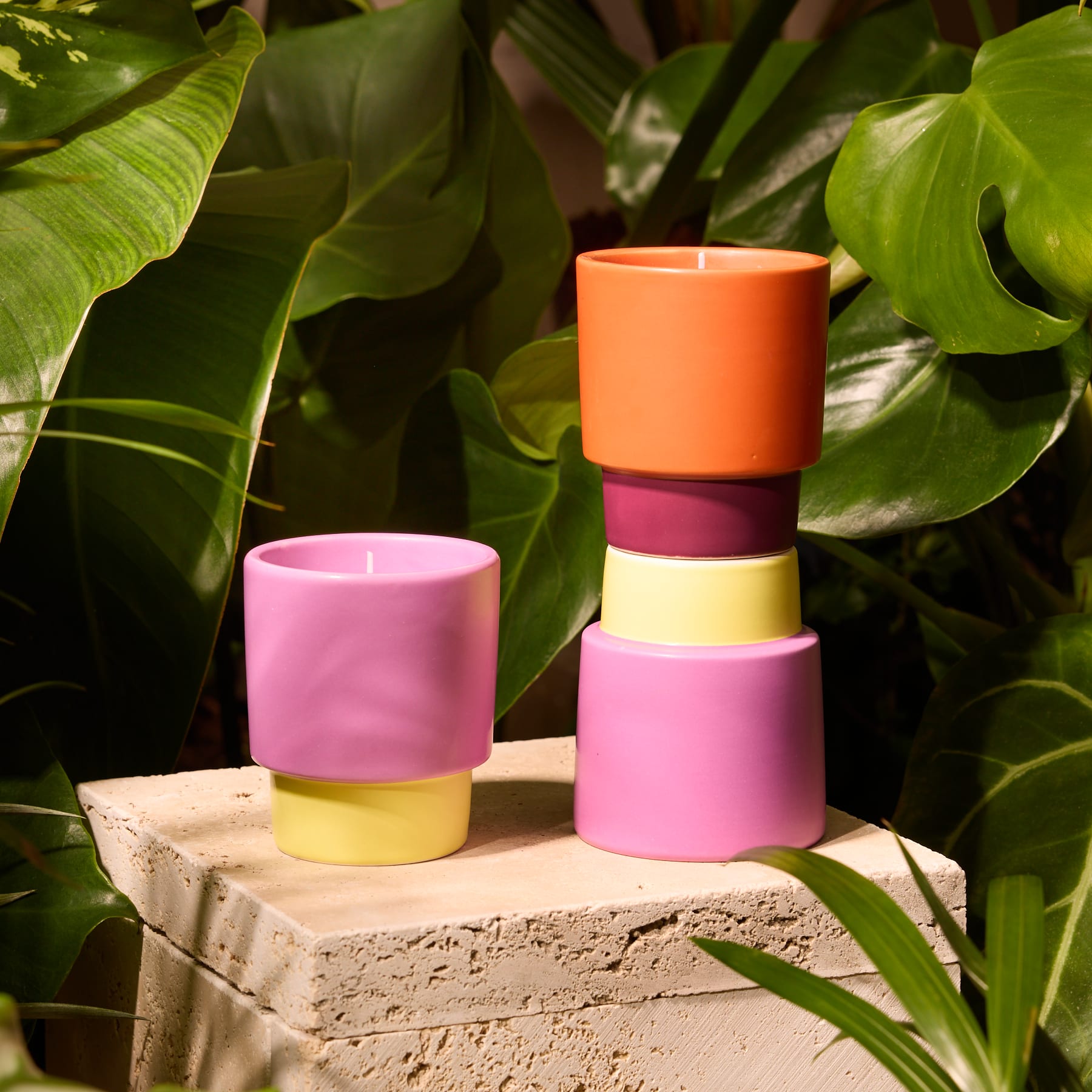 Auf einer hellen Fläche stehen zwei bunte Kerzenhalter in verschiedenen Rosa-, Orange- und Gelbtönen.