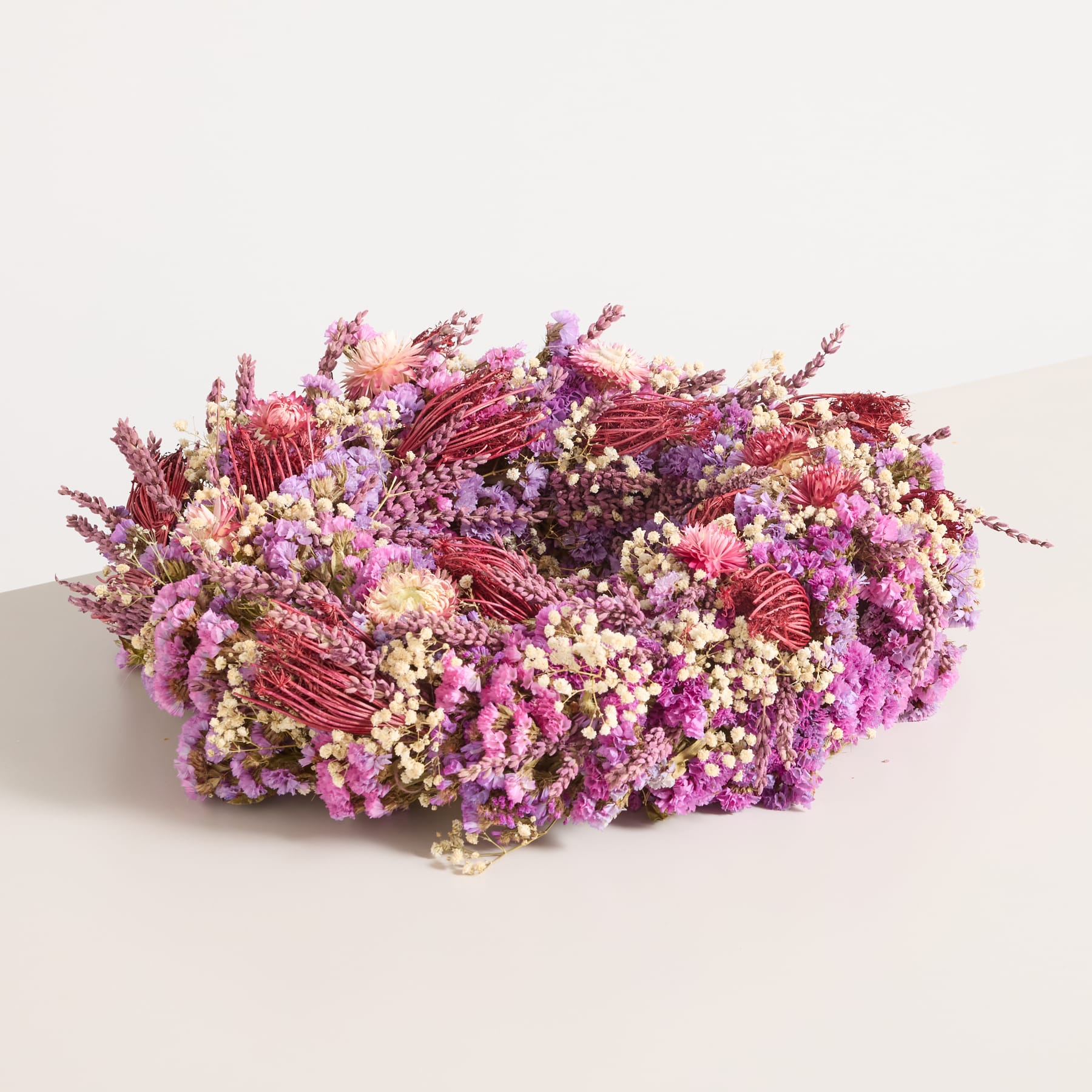 Ein lebendiges und farbenfrohes Blumenarrangement aus Blumen in verschiedenen Rosa- und Lilatönen, darunter scheinbar getrocknete Blumen oder Blätter, die auf einem schlichten weißen Hintergrund ruhen.