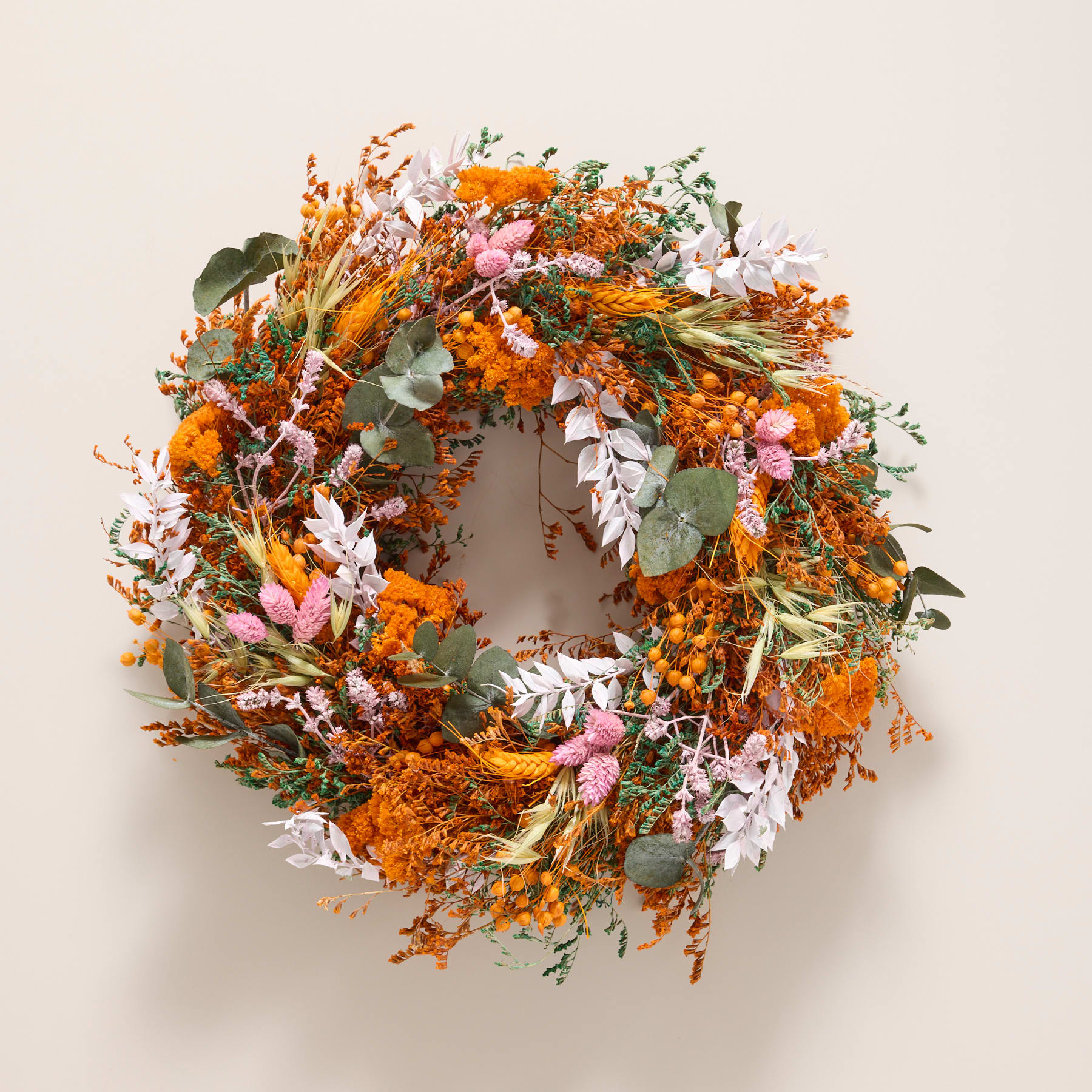 Ein lebendiger und farbenfroher Kranz aus verschiedenen getrockneten Blumen, Blättern und anderen natürlichen Elementen, präsentiert vor einem schlichten weißen Hintergrund.