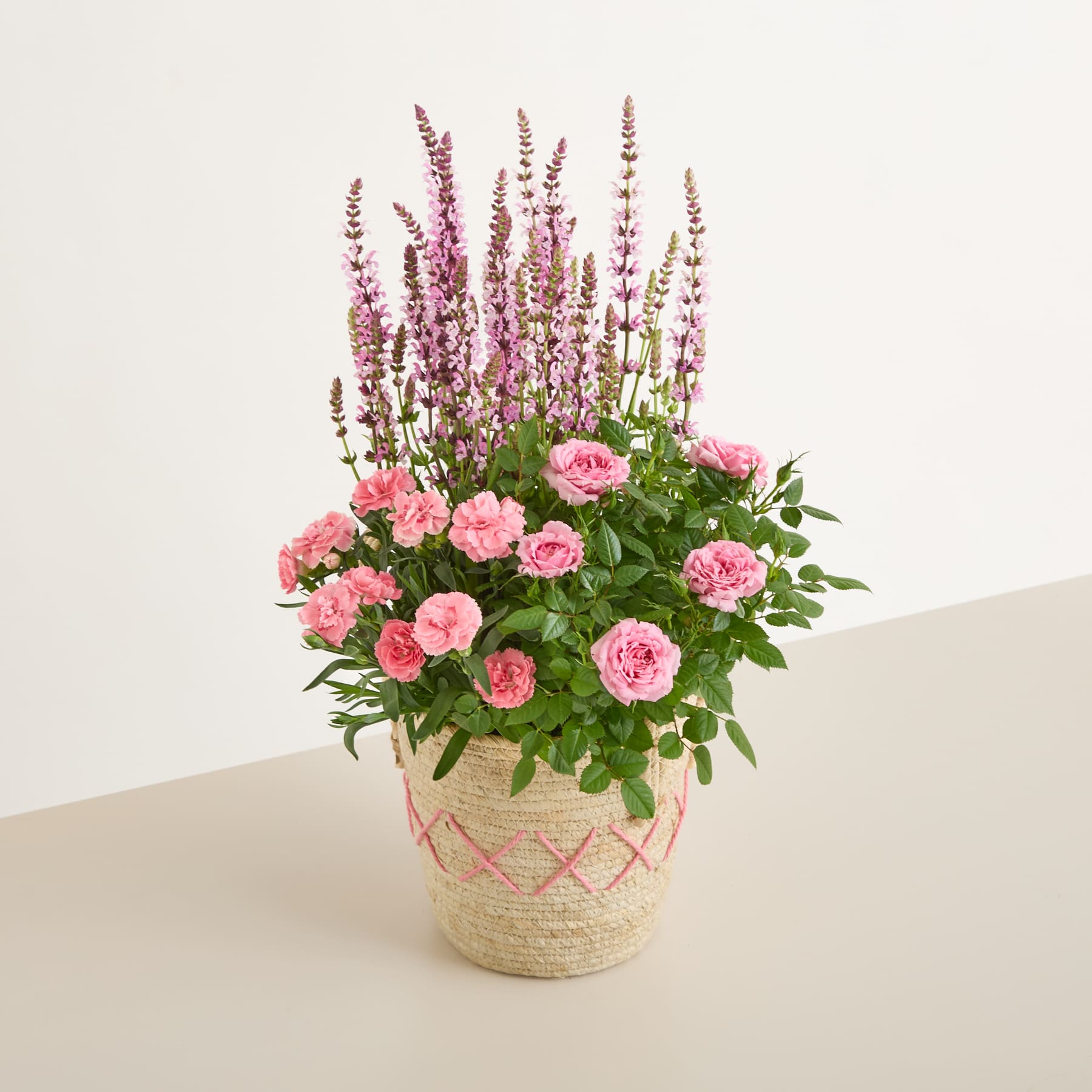 Ein Strauß leuchtend rosa Rosen und violetter Lavendelblüten, arrangiert in einem geflochtenen Korb, den eine Person vor einem schlichten blauen Hintergrund in den Händen hält.