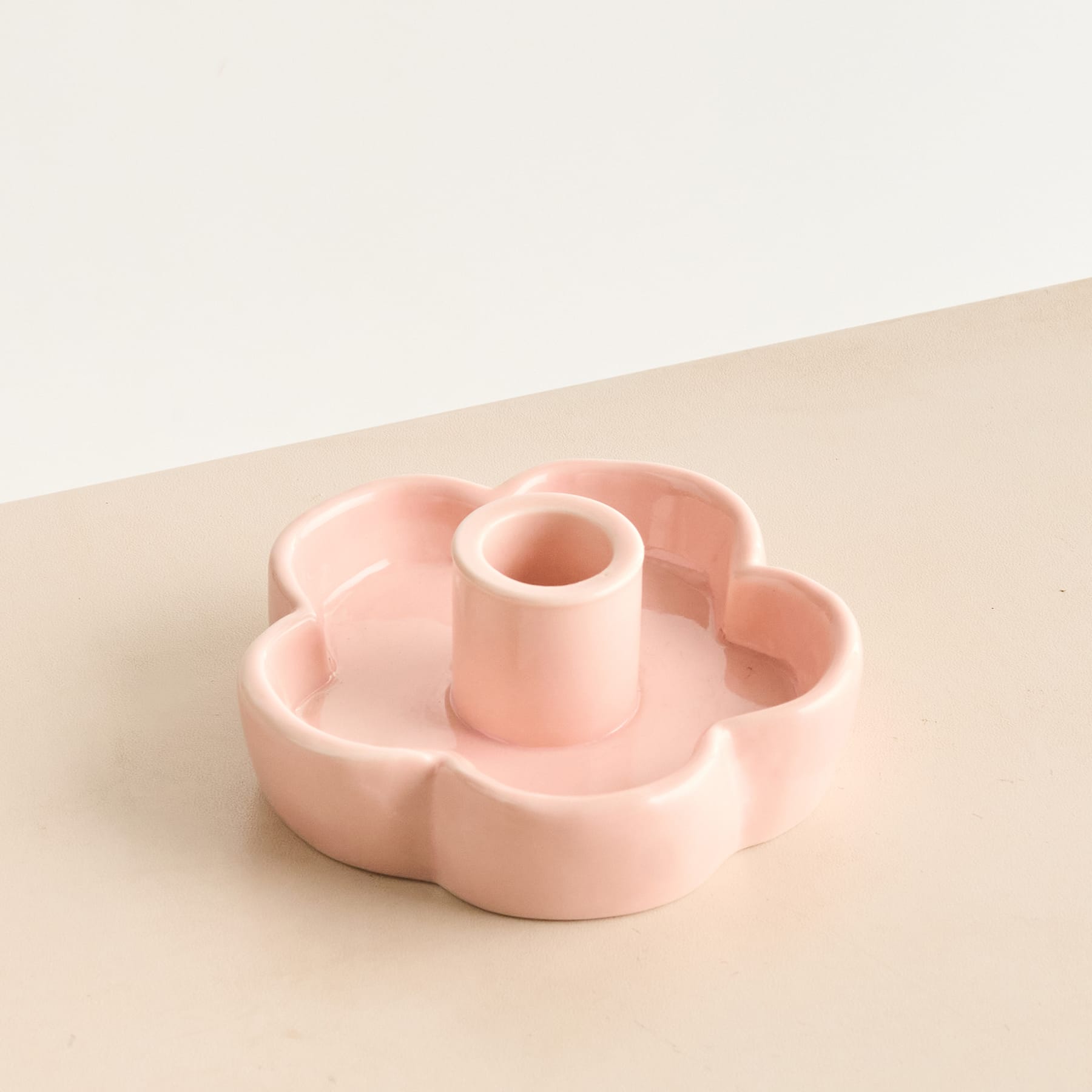 Ein zarter, pastellfarbener Kerzenhalter aus Keramik in Blumenform steht auf einer schlichten, hellen Oberfläche.