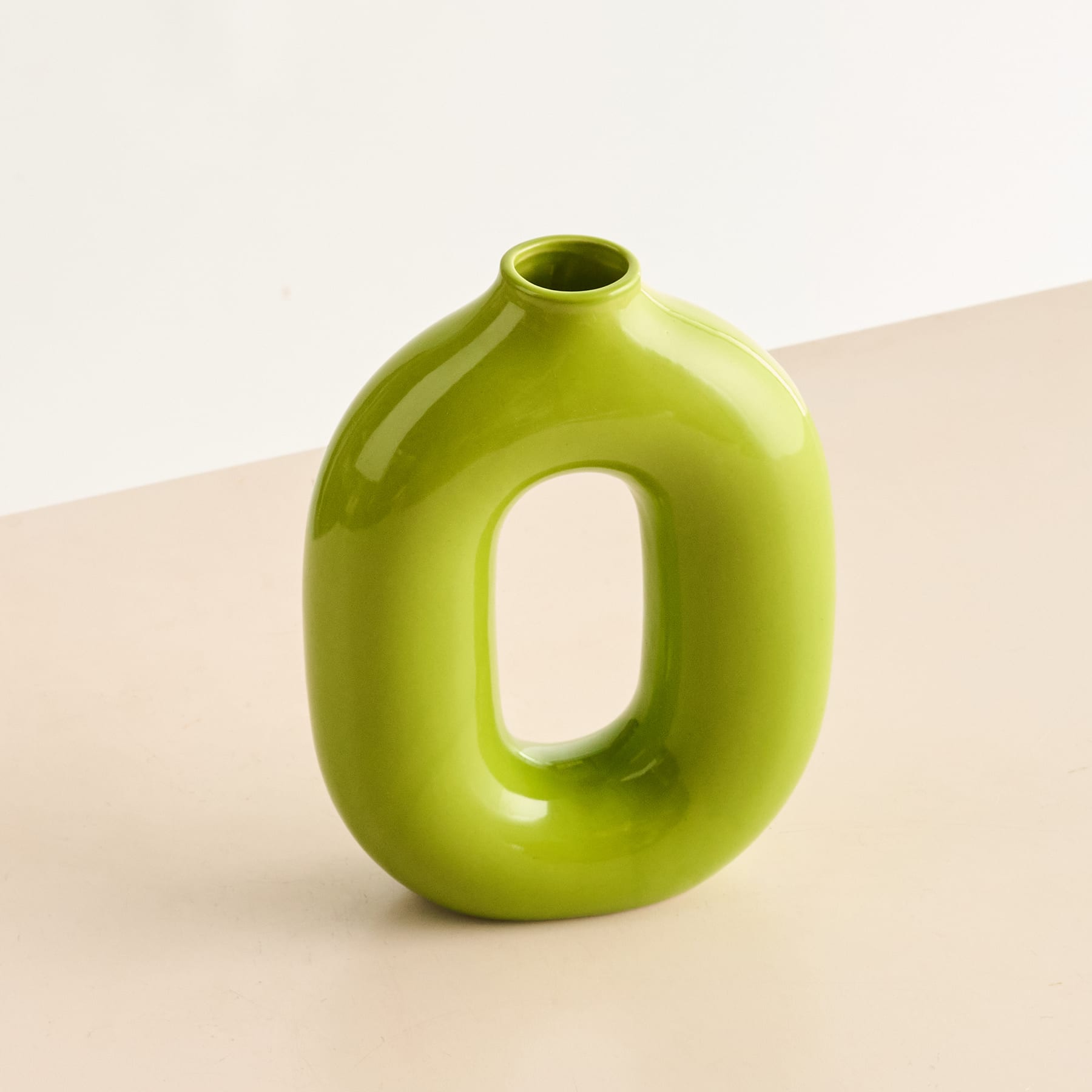 Eine leuchtend grüne Keramikvase mit einer einzigartigen, abstrakten Form steht auf einer neutral getönten Oberfläche vor einem schlichten Hintergrund.
