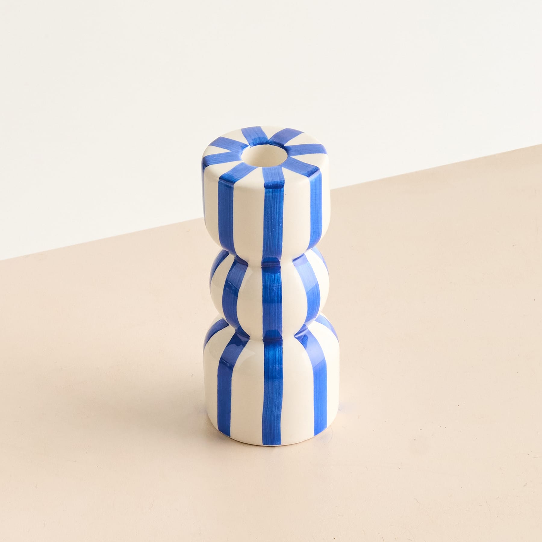 Ein blau-weiß gestreiftes zylindrisches Objekt mit einer blumenähnlichen Form auf der Oberseite liegt auf einer beigen Oberfläche vor einem schlichten Hintergrund.