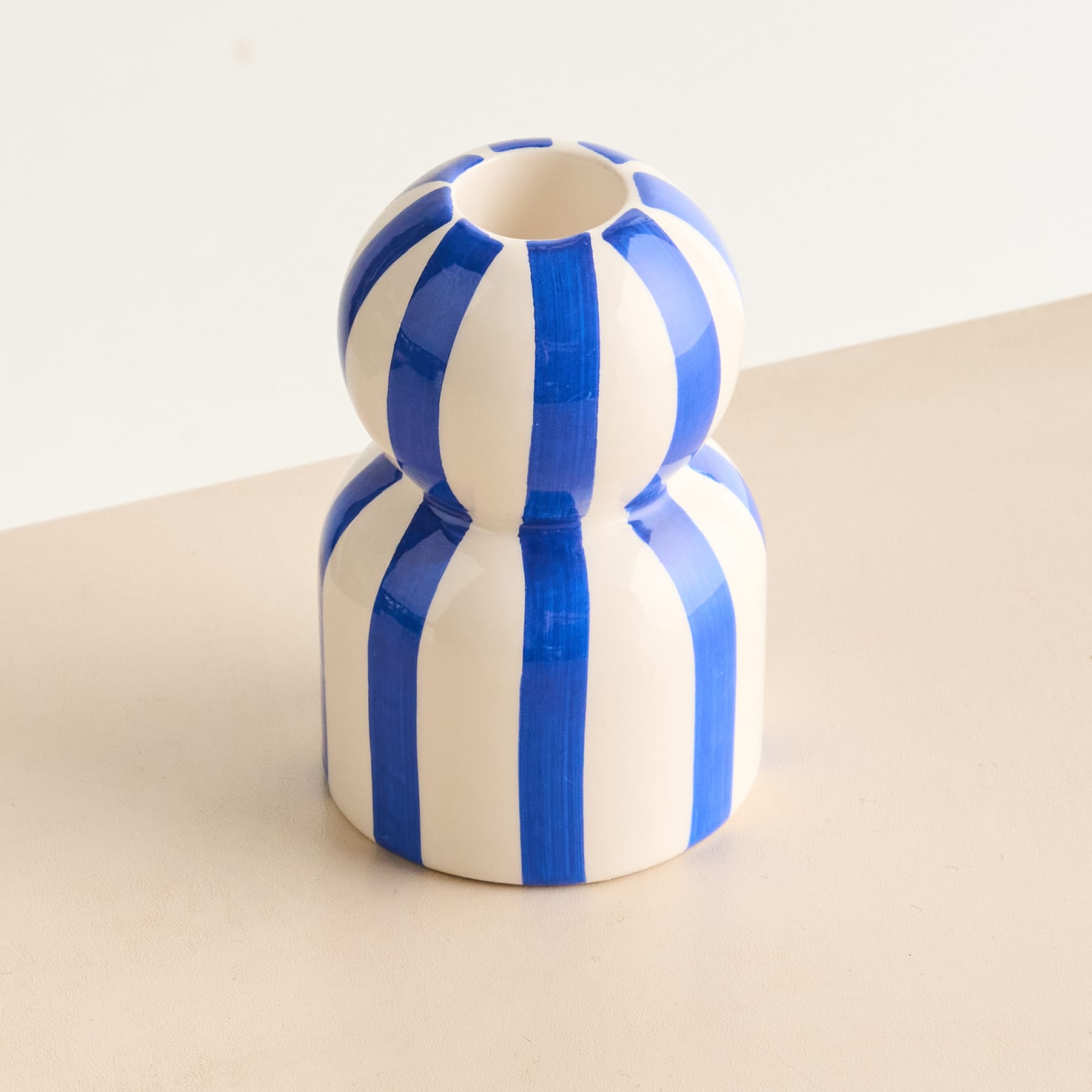 Eine blau-weiß gestreifte Keramikfigur sitzt auf einer beigen Oberfläche vor einem schlichten Hintergrund.