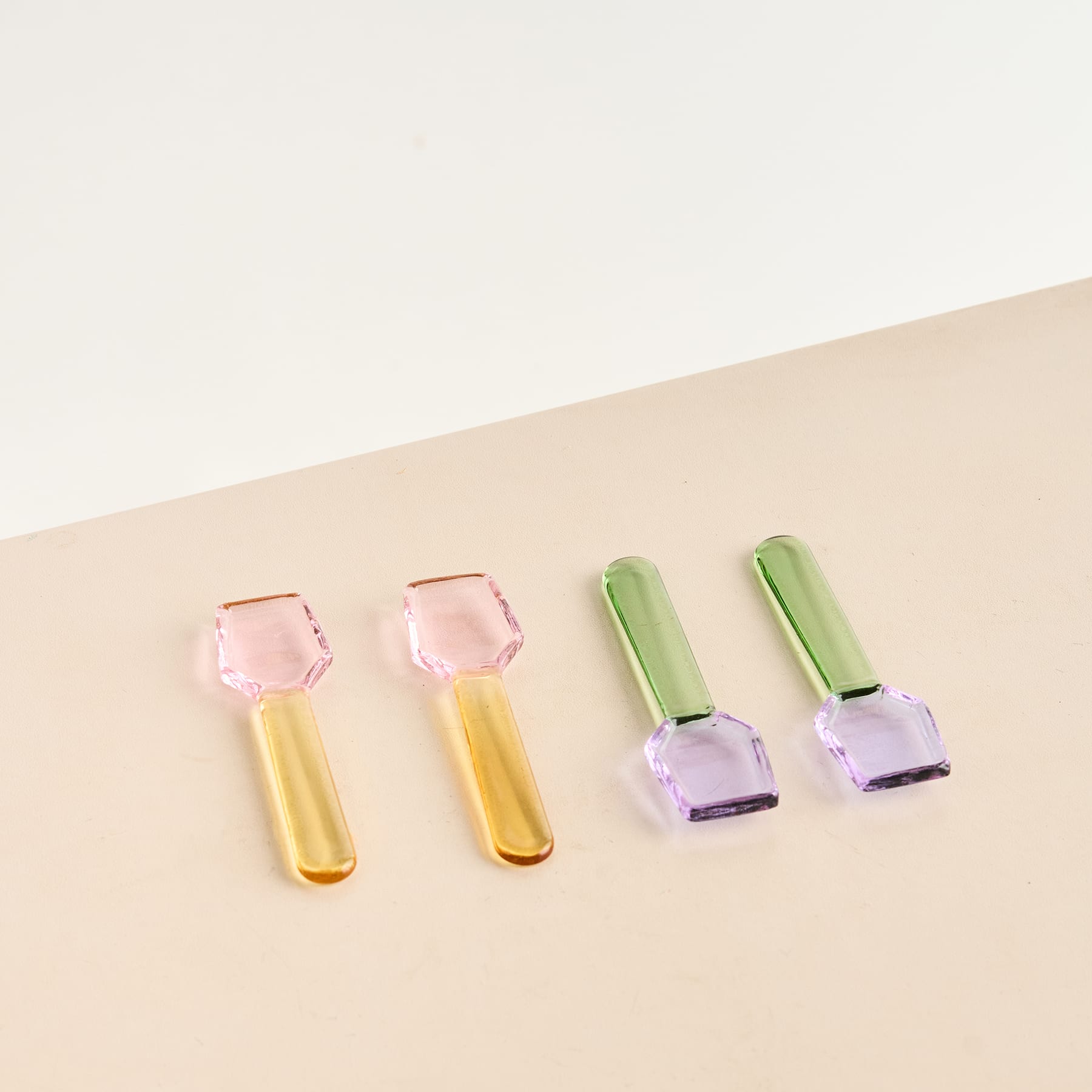 Das Bild zeigt vier bunte Beauty-Tools, darunter zwei rosa-goldene Gesichtsroller und zwei lila-grüne Nagellackflaschen, angeordnet auf einem hellen Hintergrund.