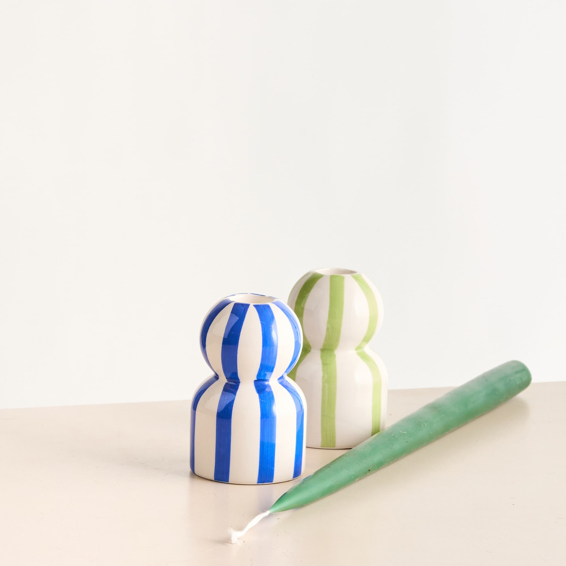 Das Bild zeigt zwei bunte Holzfiguren und einen grünen Bleistift auf einem hellen Untergrund.