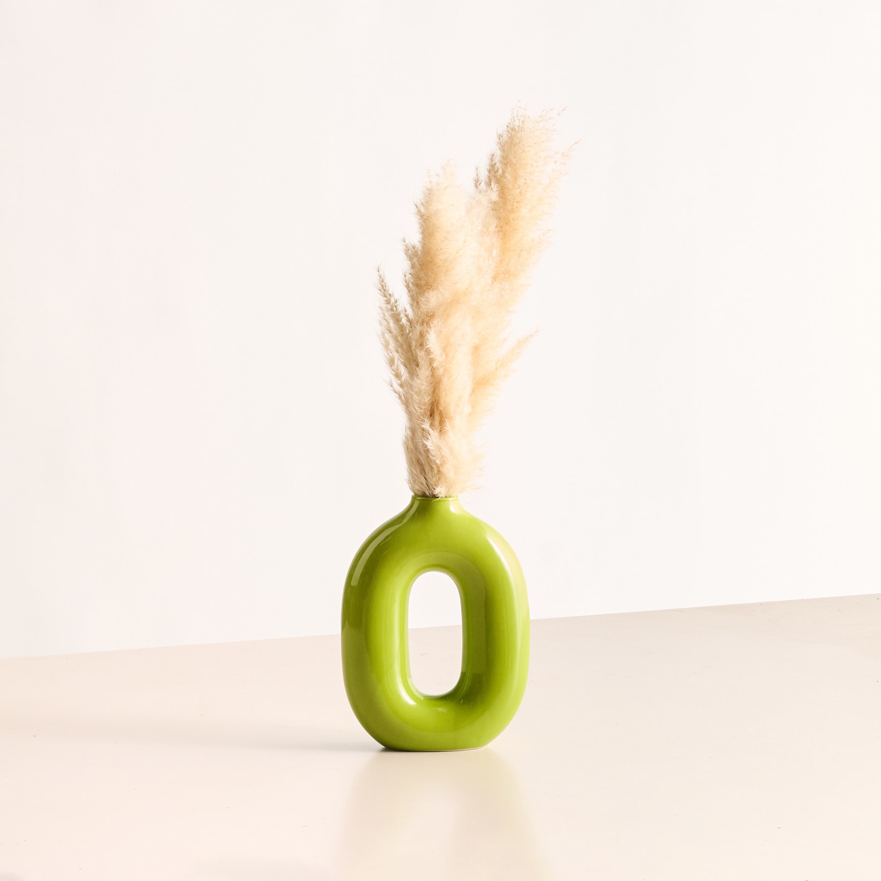 Eine leuchtend grüne Keramikvase hält eine zarte Pampasgrasfeder vor einem schlichten weißen Hintergrund.