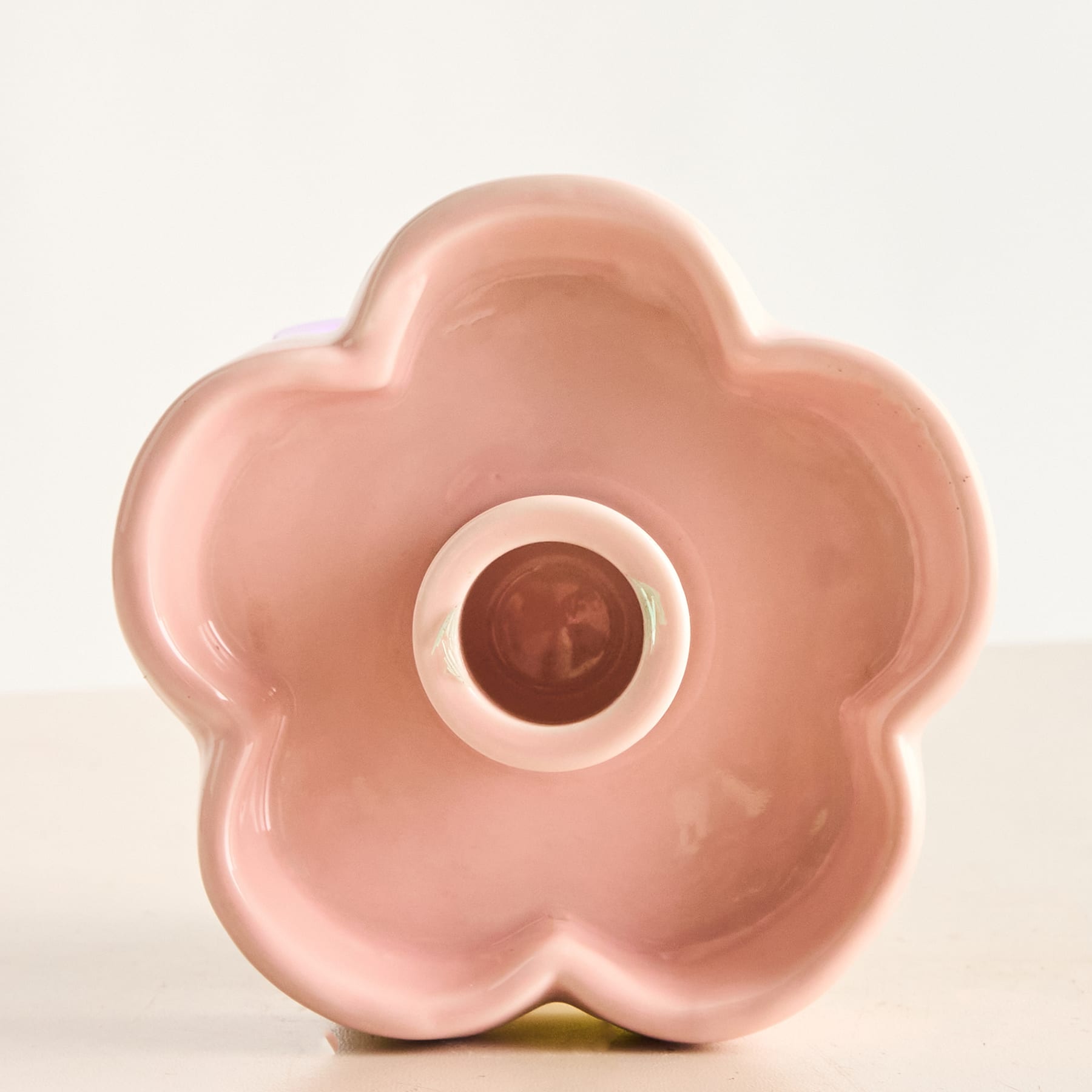 Eine rosafarbene Vase oder ein rosafarbener Behälter aus Keramik in Blumenform steht auf einem schlichten weißen Hintergrund.
