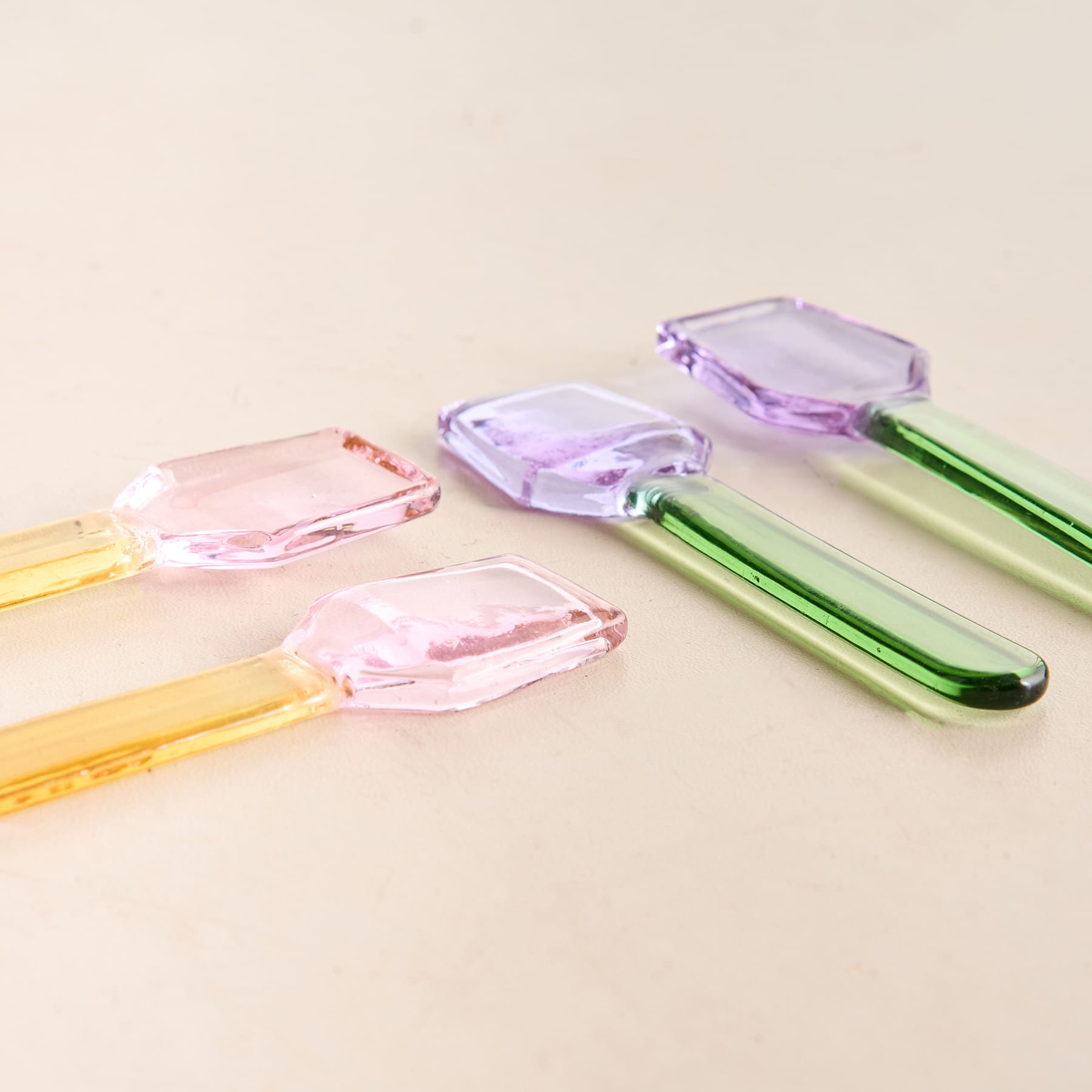 Das Bild zeigt mehrere bunte Glas- oder Kristallobjekte, darunter einige durchscheinende, geometrische Formen in Rosa-, Lila- und Grüntönen, die auf einer hellen Oberfläche angeordnet sind.