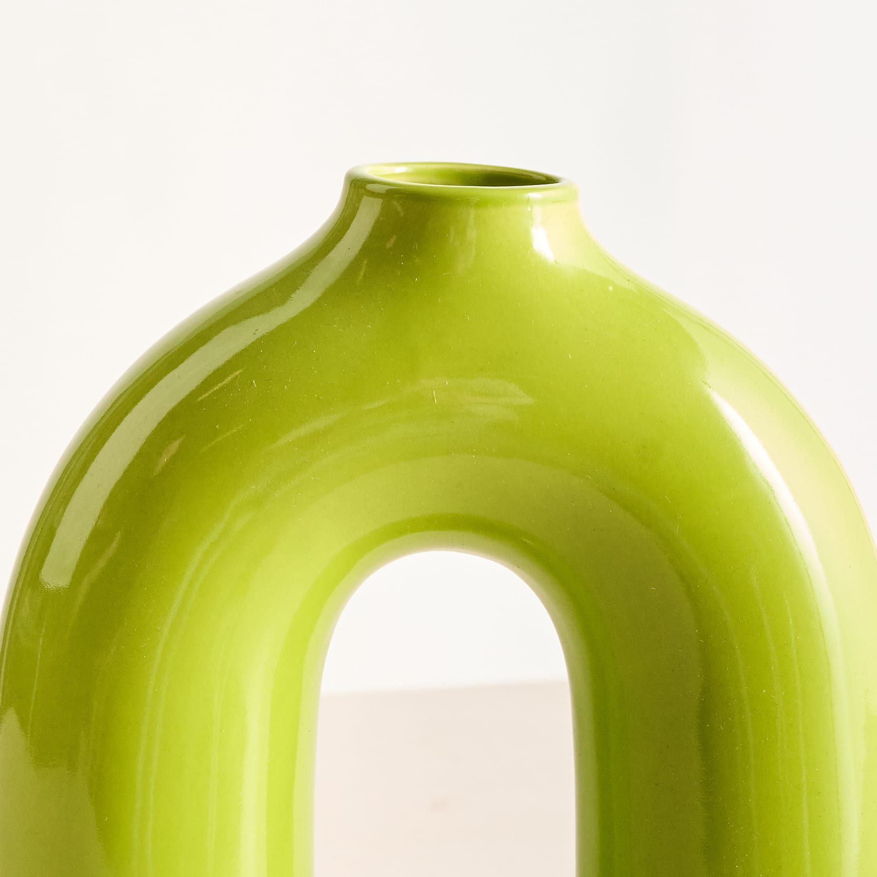Eine leuchtend grüne Keramikvase mit einer einzigartigen, geschwungenen Form und einer offenen Mitte steht vor einem schlichten weißen Hintergrund.
