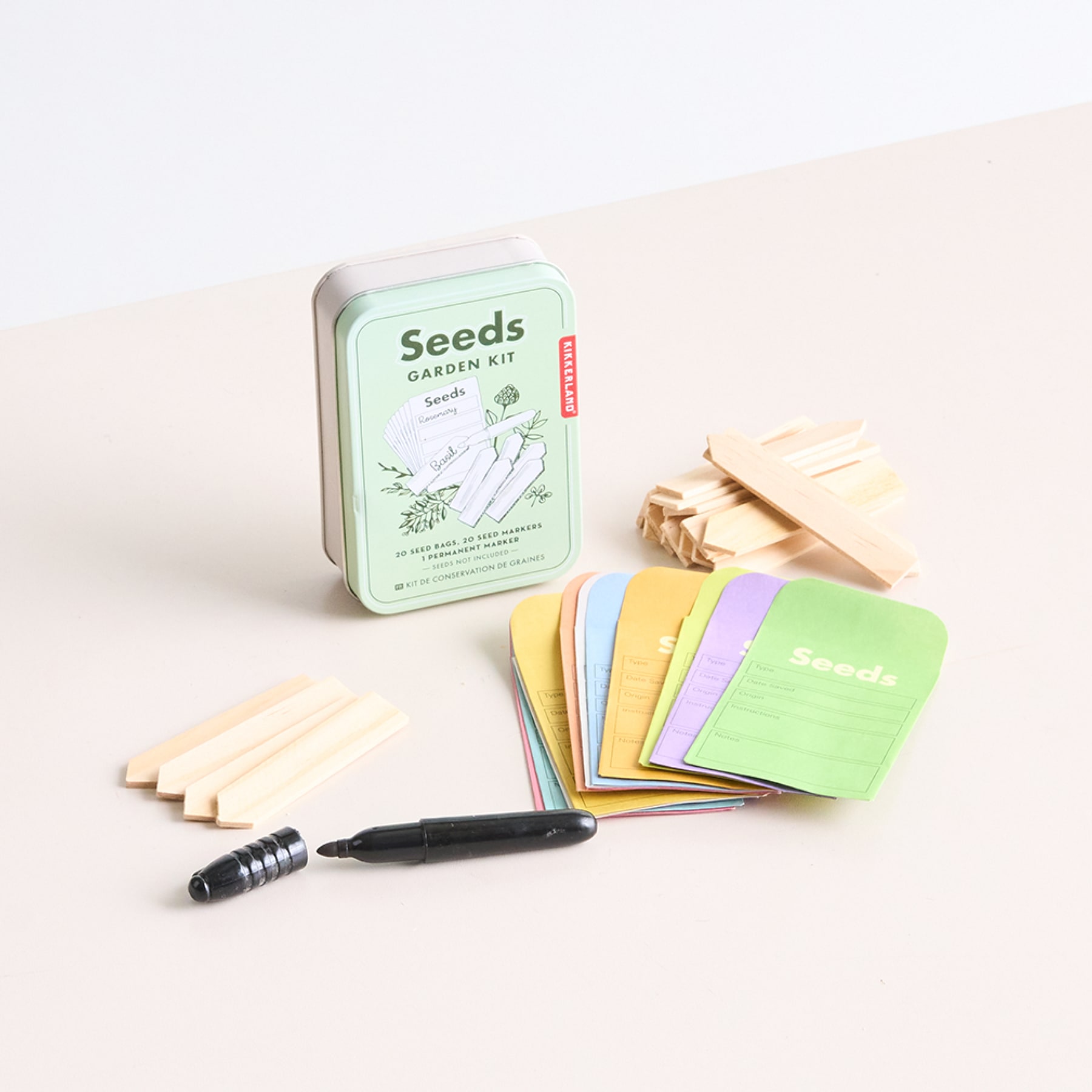 Eine Sammlung von Gartenbedarf, darunter ein Samenpaket, hölzerne Pflanzenmarkierungen und ein kleiner grüner Behälter, angeordnet auf einer hellen Oberfläche.