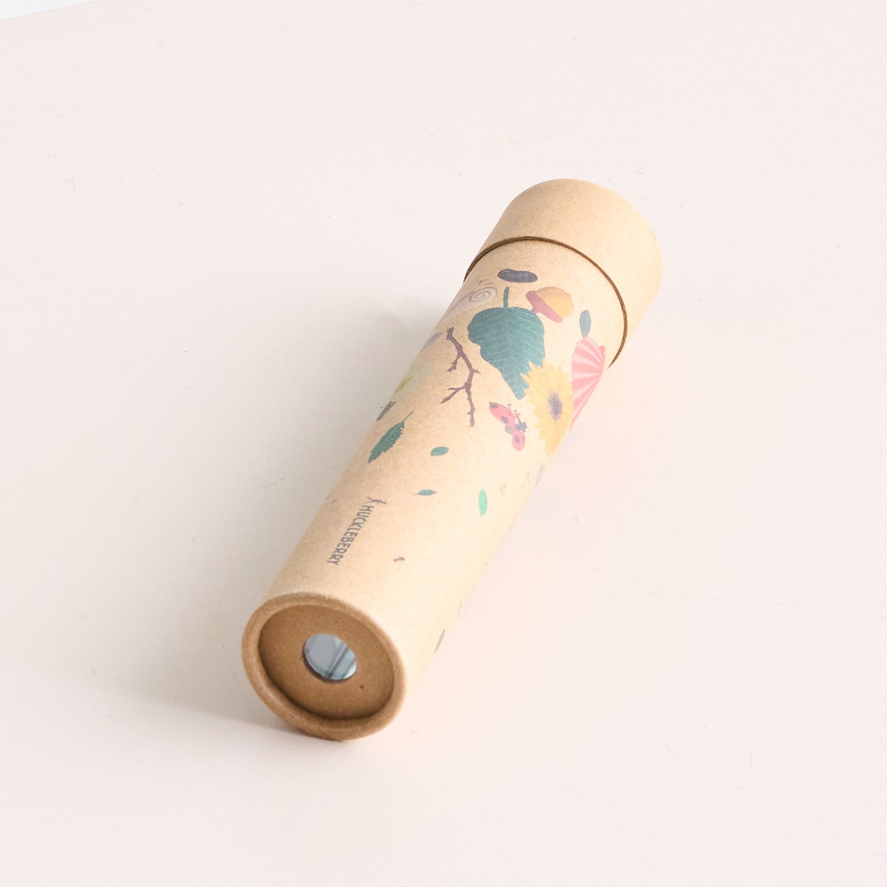 Ein kaleidoskopartiges Holzobjekt mit einem bunten, gesprenkelten Muster liegt auf einer schlichten, hellen Oberfläche.