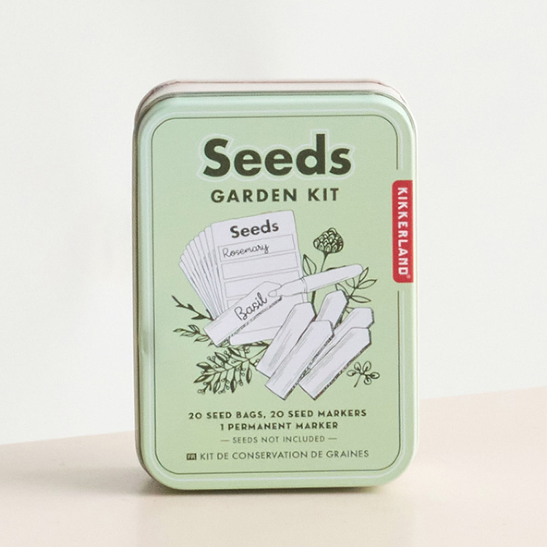 Ein grüner Blechbehälter mit der Aufschrift „Seeds“ steht auf einer hellen Oberfläche vor einem schlichten weißen Hintergrund.