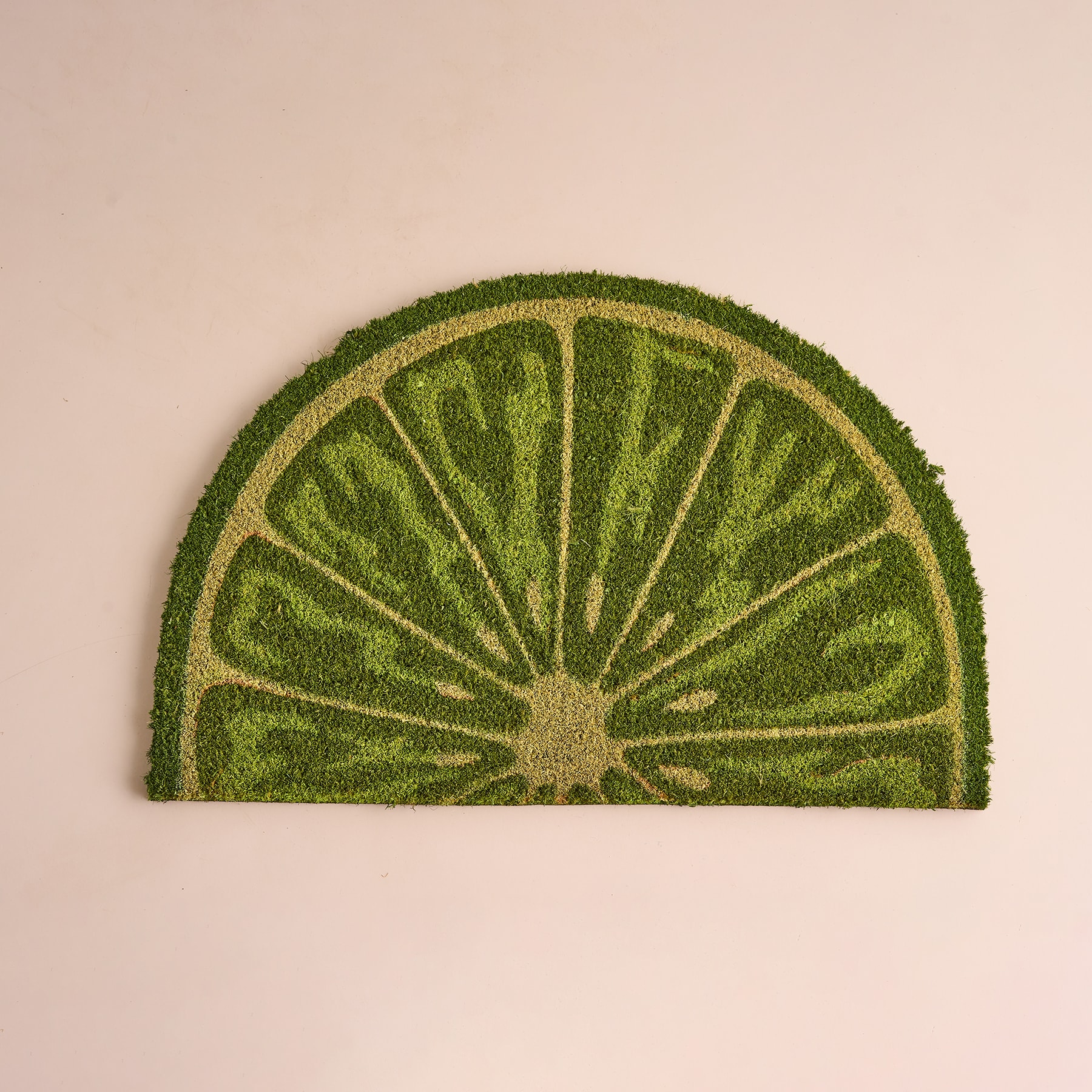 Eine halbe Limetten- oder Zitronenscheibe aus grünem Moos oder Gras vor einem hellpfirsichfarbenen Hintergrund.
