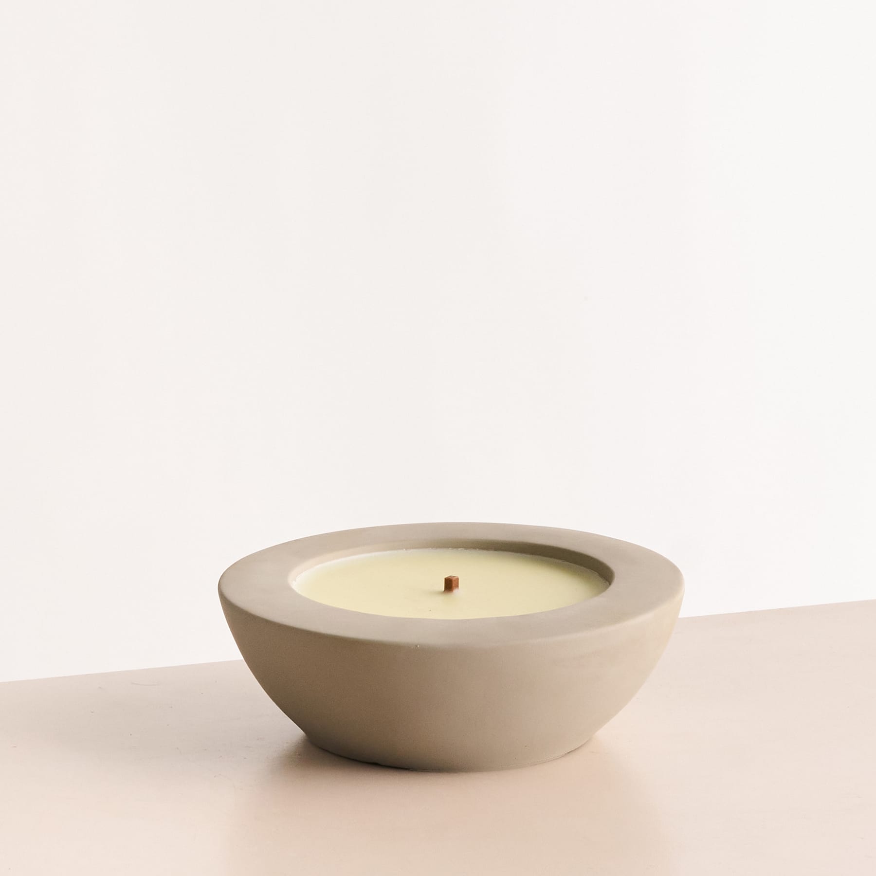 Eine einfache, minimalistische Keramikschale mit einer brennenden Kerze auf einer schlichten, hellen Oberfläche.