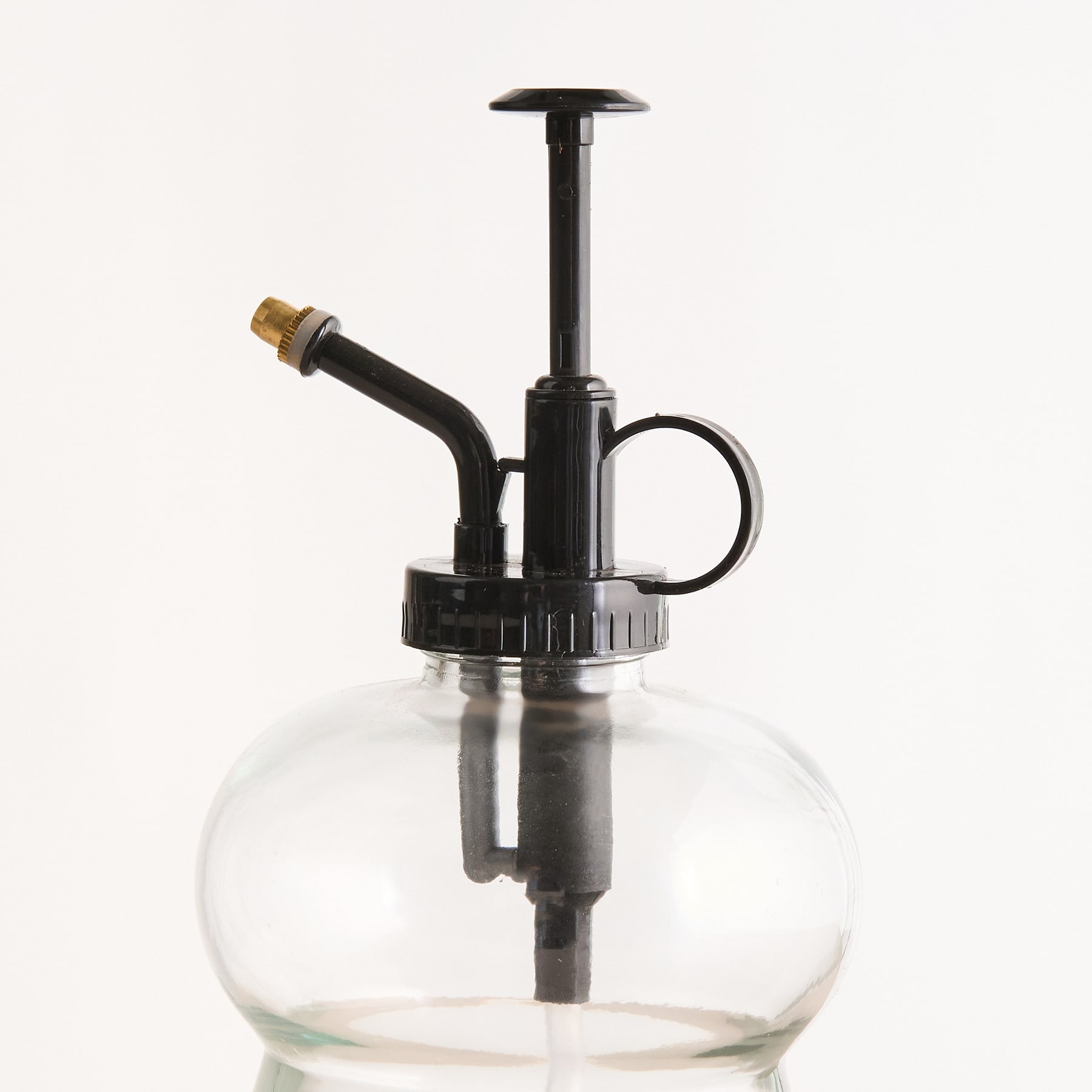 Ein durchsichtiger Glasbehälter mit einem Pumpmechanismus aus schwarzem Metall und einer messingfarbenen Düse vor einem schlichten weißen Hintergrund.