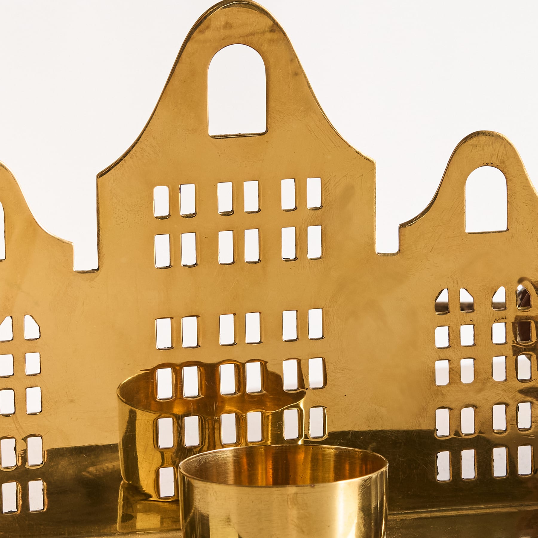 Im Vordergrund steht vor einem schlichten weißen Hintergrund eine goldene, architektonische Struktur mit komplizierten Ausschnitten, die einem Miniaturgebäude ähnelt.