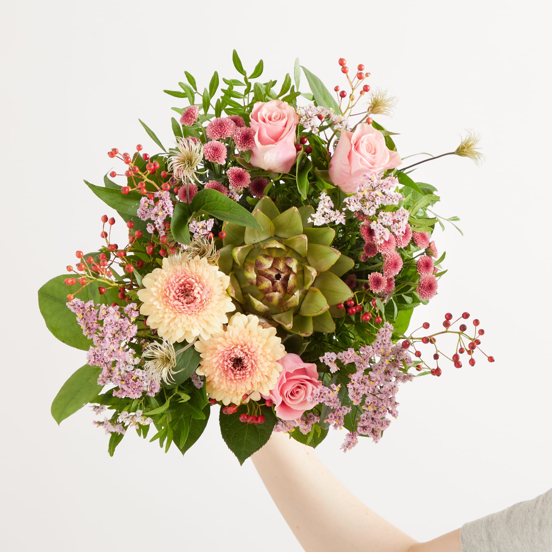 Ein farbenfroher Strauß verschiedener Blumen, darunter rosa Rosen, gelbe Gänseblümchen und eine grüne Sukkulente, arrangiert in einer Vase vor einem schlichten weißen Hintergrund.
