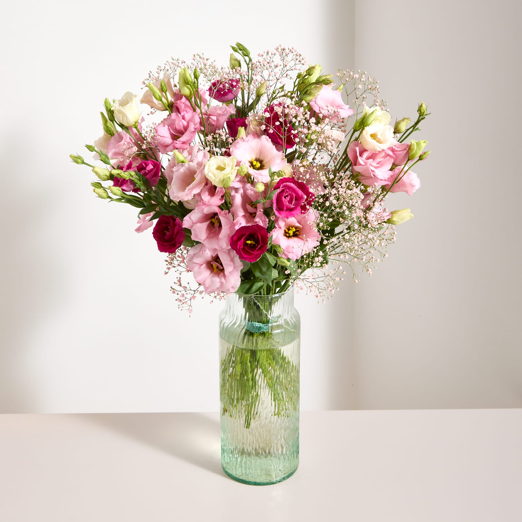 Ein farbenfroher Strauß rosa und weißer Blumen, darunter Rosen und Schleierkraut, wird vor einem schlichten grauen Hintergrund in der Hand einer Person gehalten.