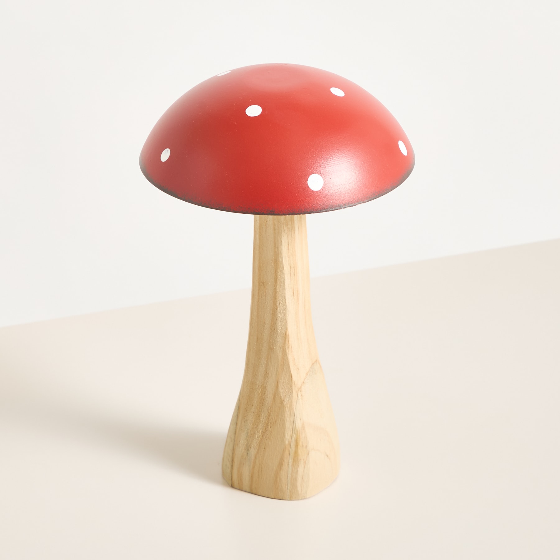 Ein leuchtend rotes, pilzförmiges Objekt mit weißen Punkten sitzt auf einem Holzstiel vor einem schlichten weißen Hintergrund.