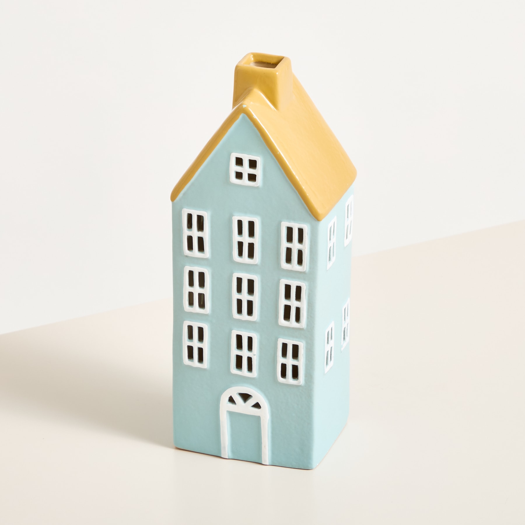 Ein Miniatur-Keramikhaus in Hellblau mit gelbem Dach auf schlichtem weißem Hintergrund.