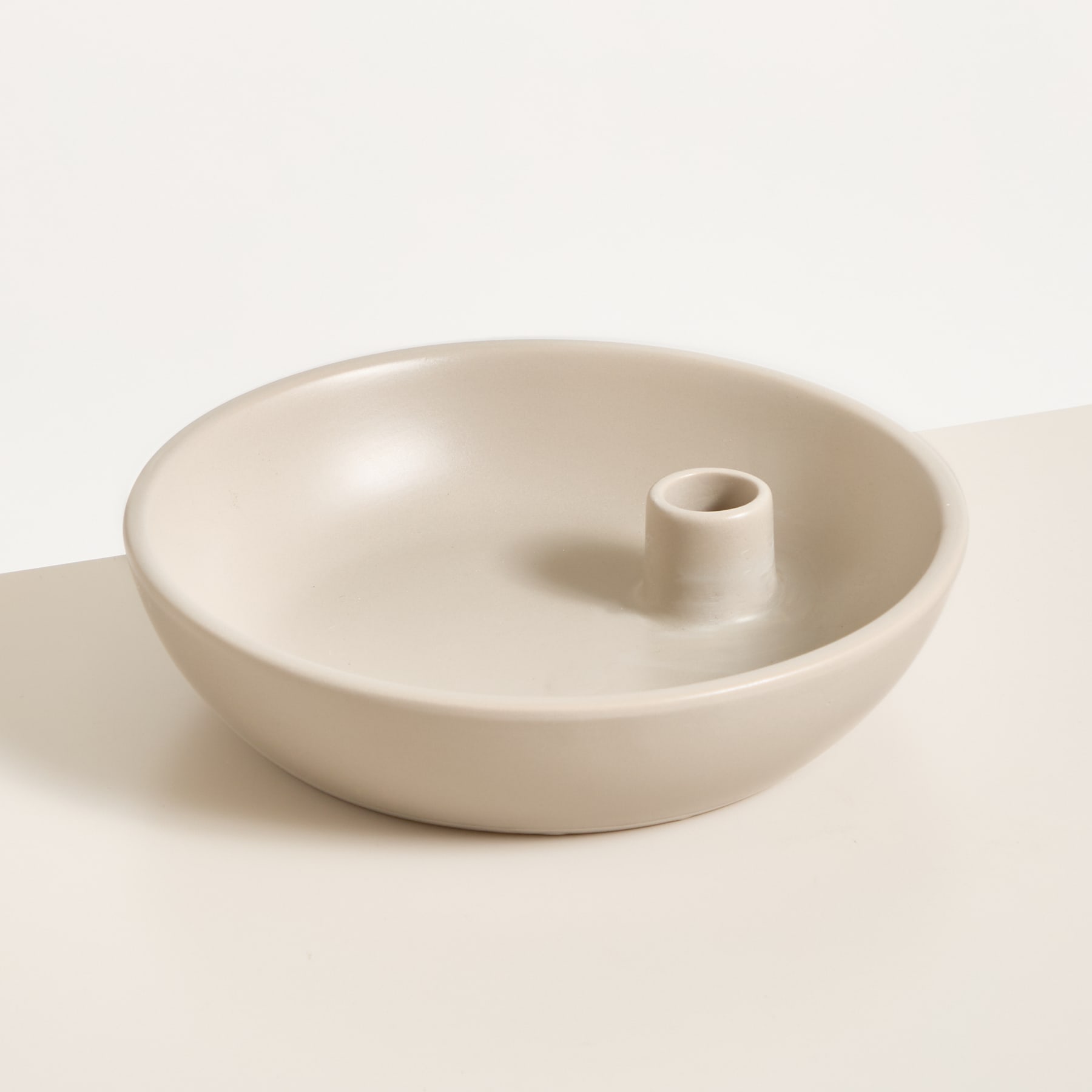 Eine einfache, minimalistische Keramikschale mit einem Loch in der Mitte steht auf einer schlichten, hellen Oberfläche.