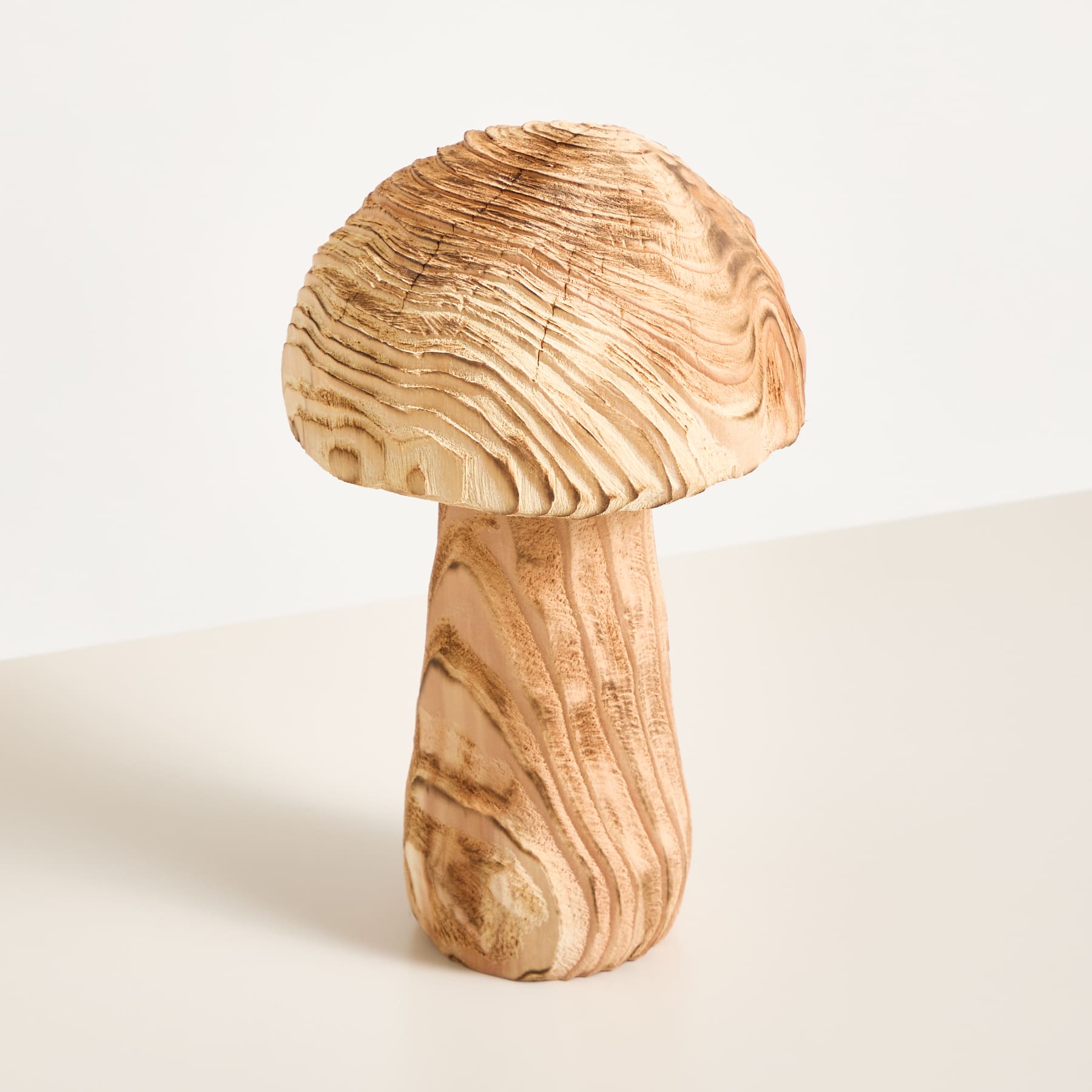 Eine pilzförmige Holzskulptur mit einem strukturierten, wirbelnden Muster steht auf einer schlichten, hellen Oberfläche.