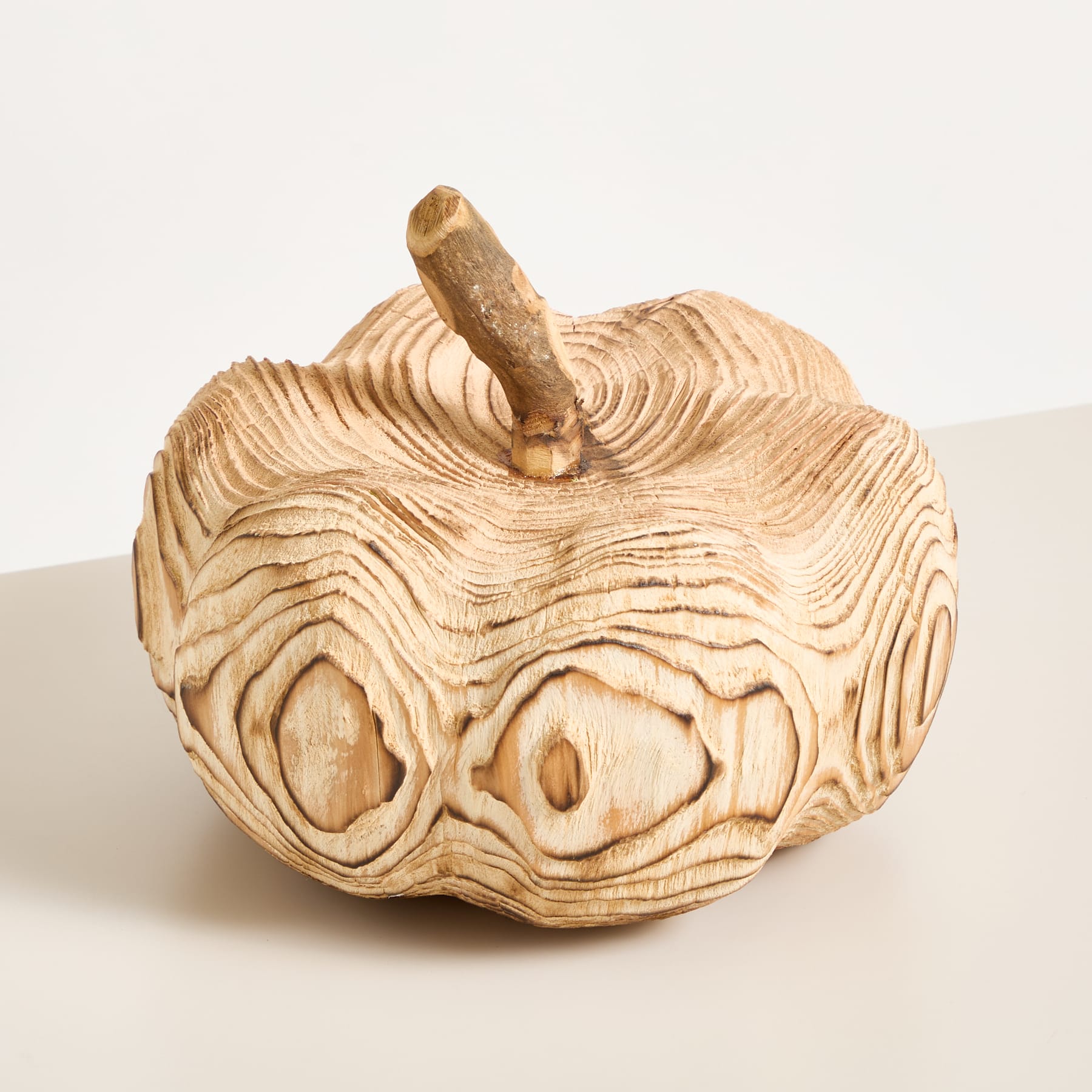 Eine apfelförmige Holzskulptur mit komplizierten, wellenförmigen Mustern, die in ihre Oberfläche geschnitzt sind, ruht auf einem schlichten, hellen Hintergrund.