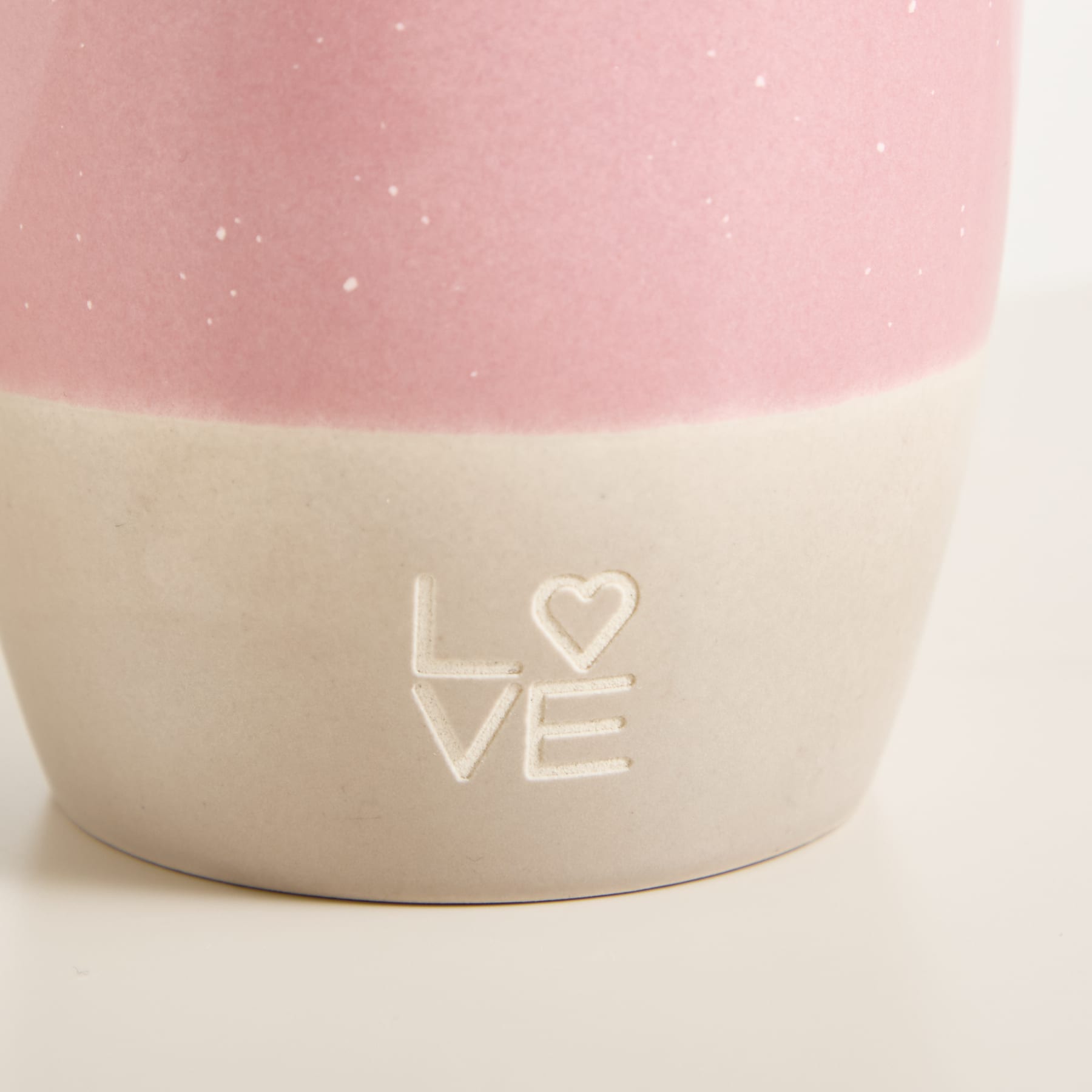 Ein rosa-weißer Keramikbehälter mit dem in die Oberfläche eingravierten Wort „LOVE“ vor einem weichen, unscharfen Hintergrund.