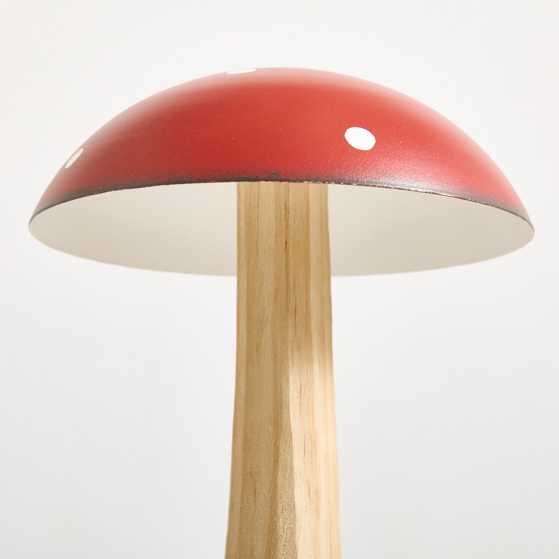 Eine leuchtend rote, pilzförmige Lampe mit Holzsockel steht vor einem schlichten weißen Hintergrund.
