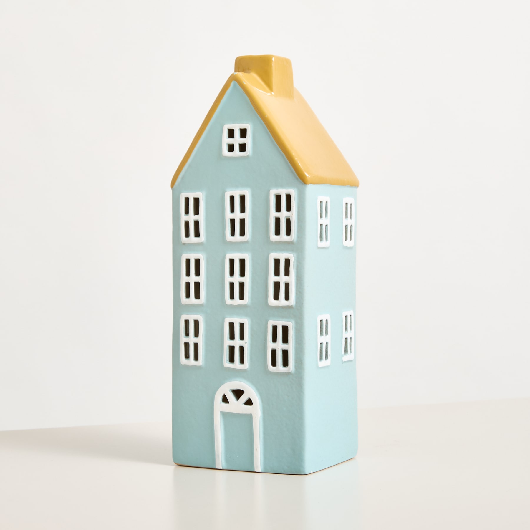 Ein Miniatur-Hausmodell aus Keramik in Hellblau mit gelbem Dach, das auf einem schlichten weißen Hintergrund steht.