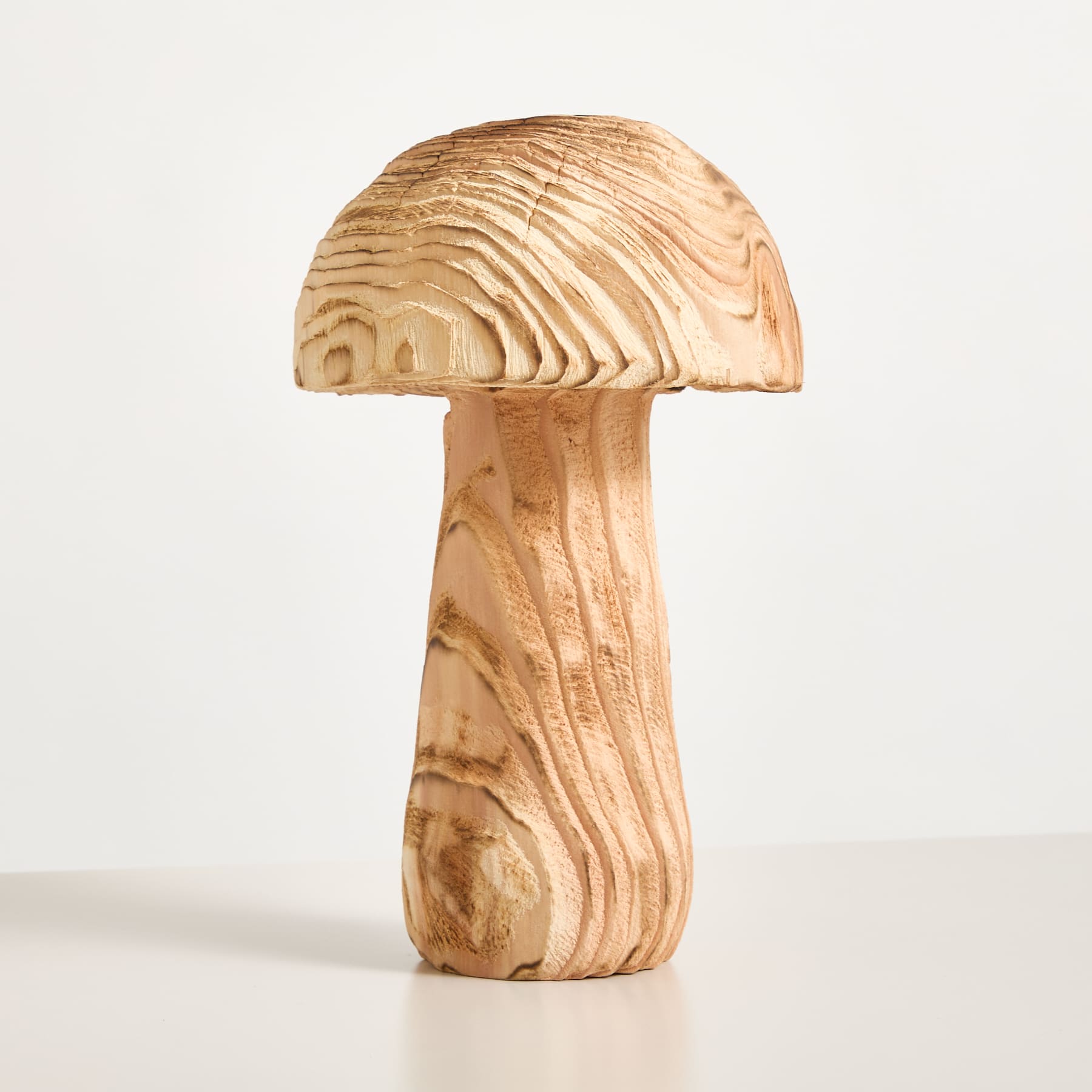 Eine pilzförmige Holzskulptur mit einer strukturierten, geschichteten Kappe steht auf einem schlichten weißen Hintergrund.