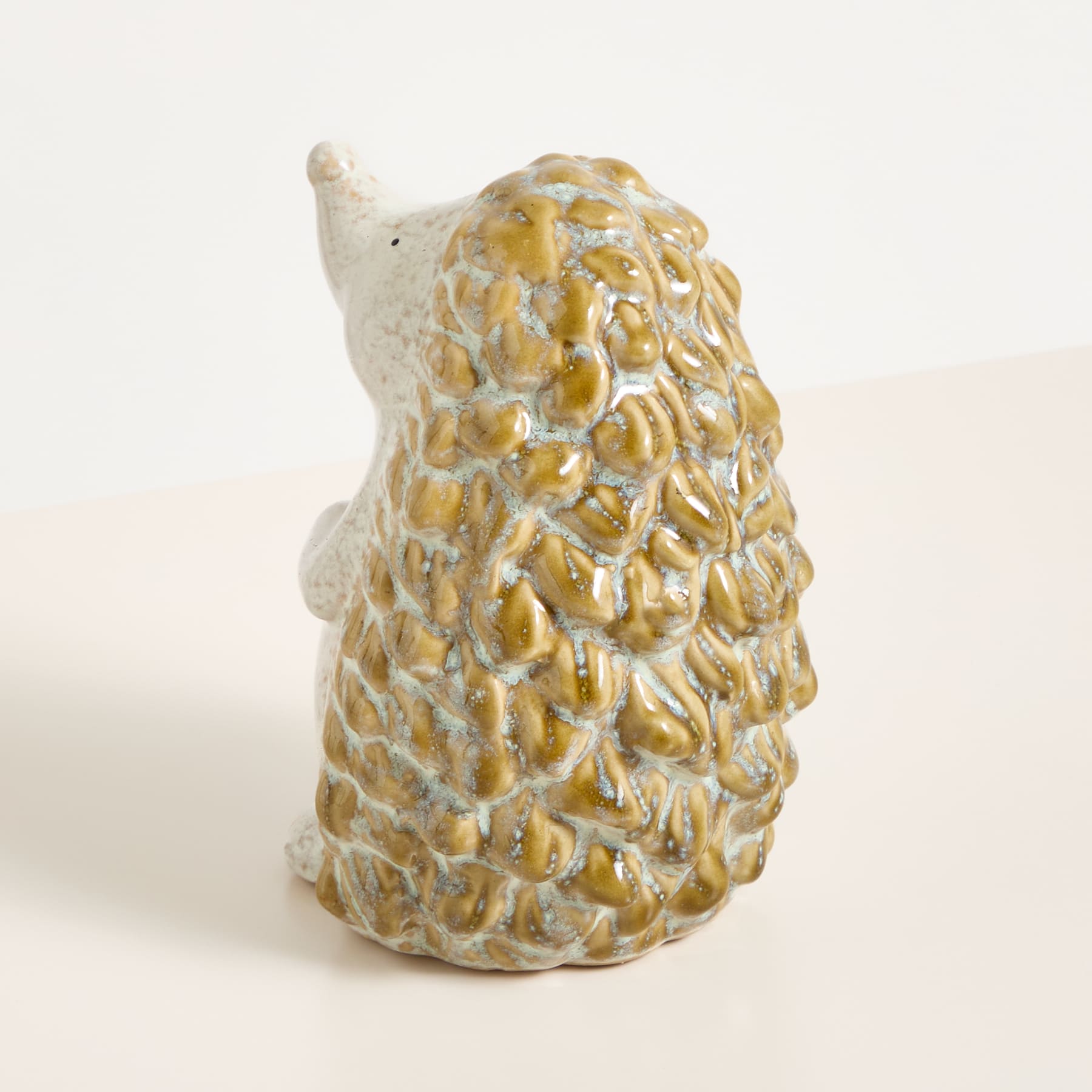Eine Keramikskulptur mit strukturierter, gemusterter Oberfläche in Beige- und Gelbtönen vor einem schlichten, hellen Hintergrund.
