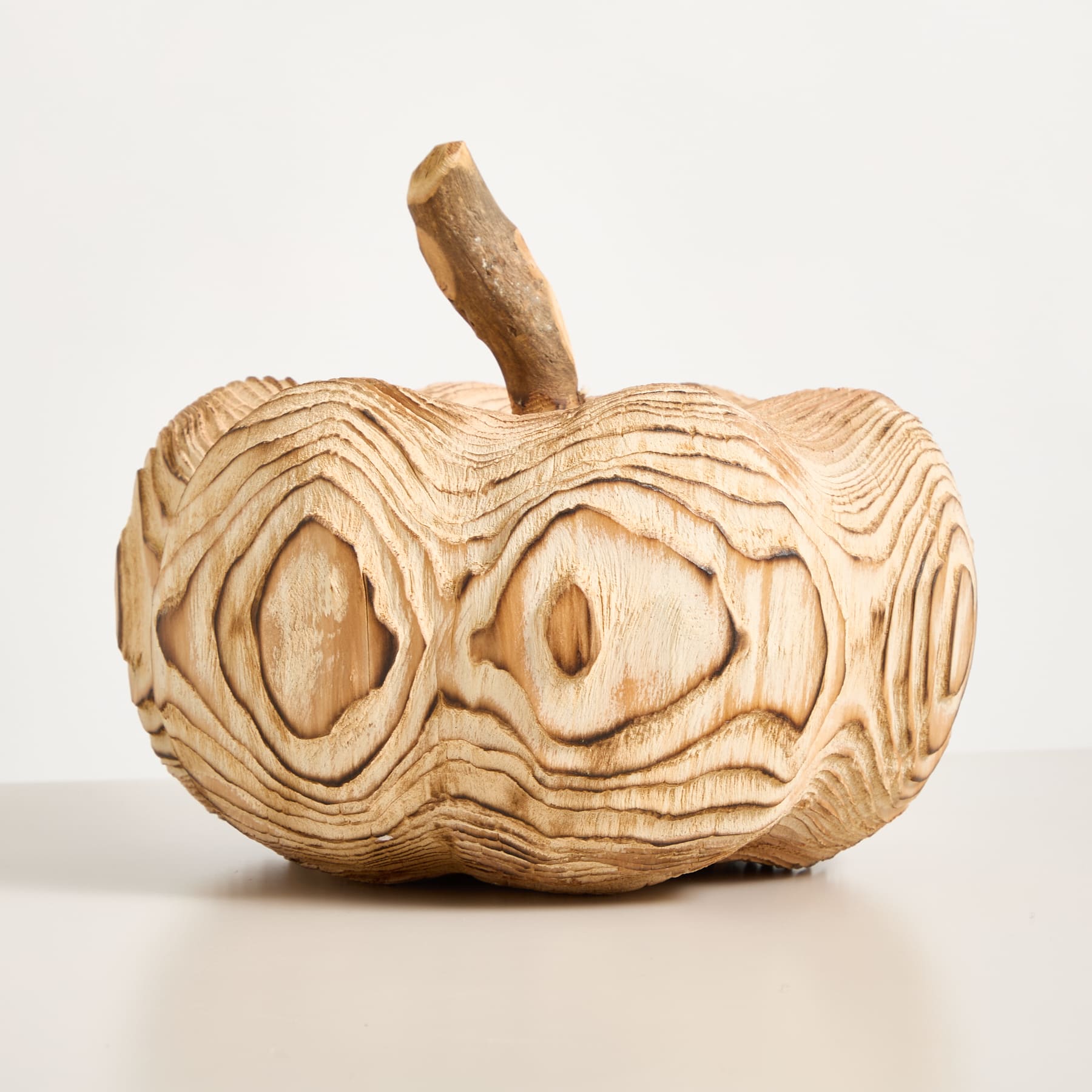 Eine apfelförmige Holzskulptur mit komplizierten, wirbelnden Mustern, die in ihre Oberfläche geschnitzt sind, vor einem schlichten weißen Hintergrund.