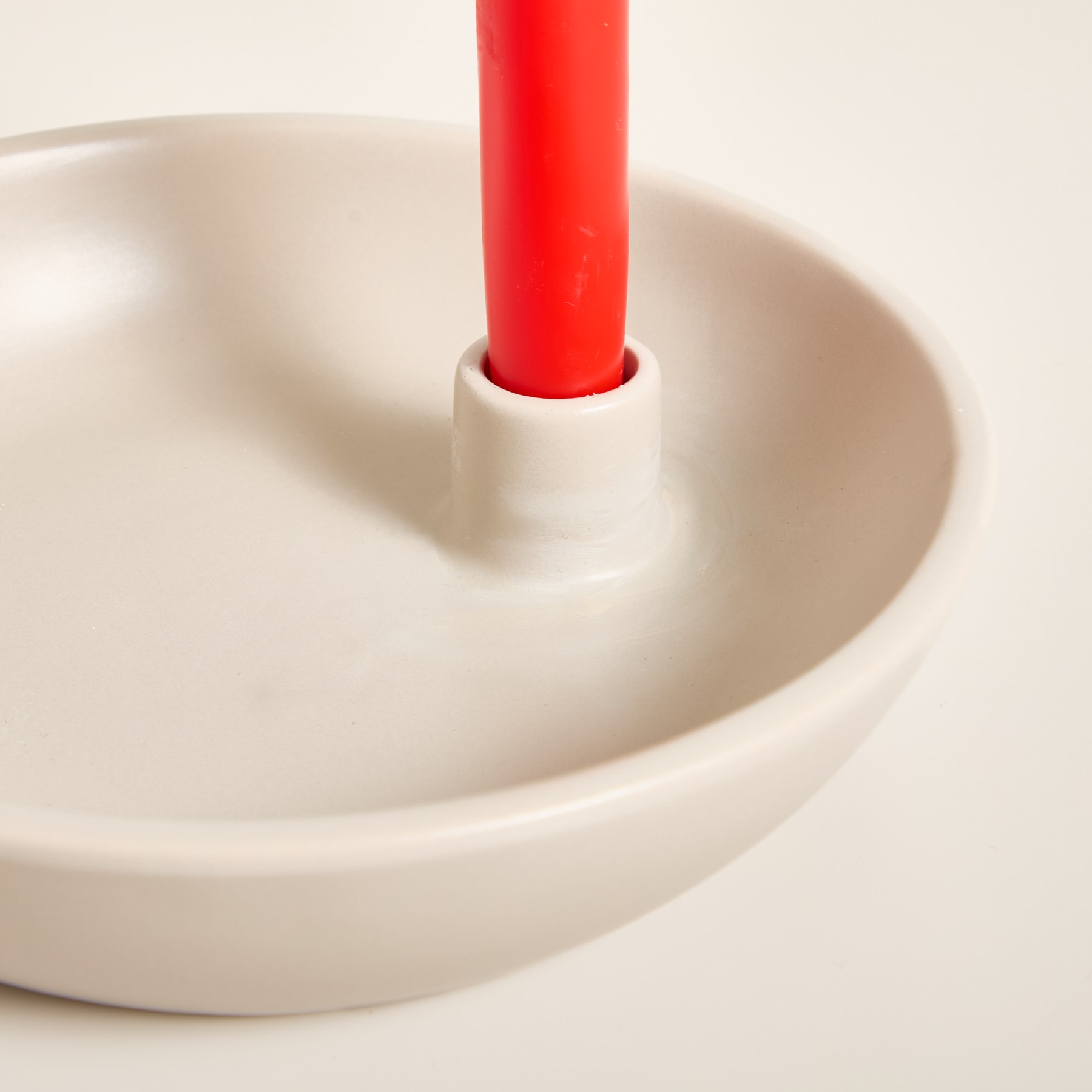 Eine rote Kerze steht aufrecht in einer weißen Keramikschale und schafft eine minimalistische und ruhige visuelle Komposition.