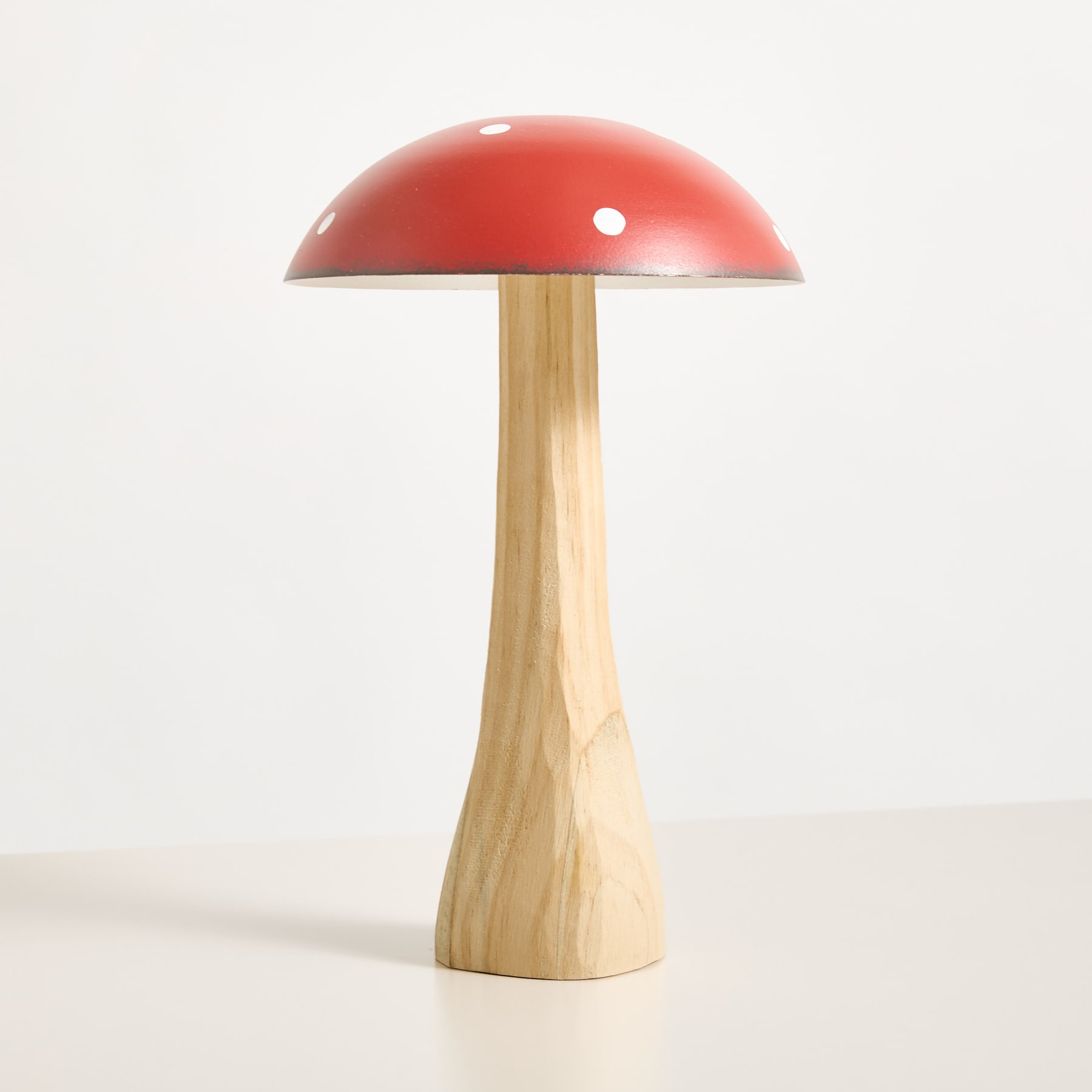 Eine rote, pilzförmige Lampe mit Holzsockel steht auf einem schlichten weißen Hintergrund.