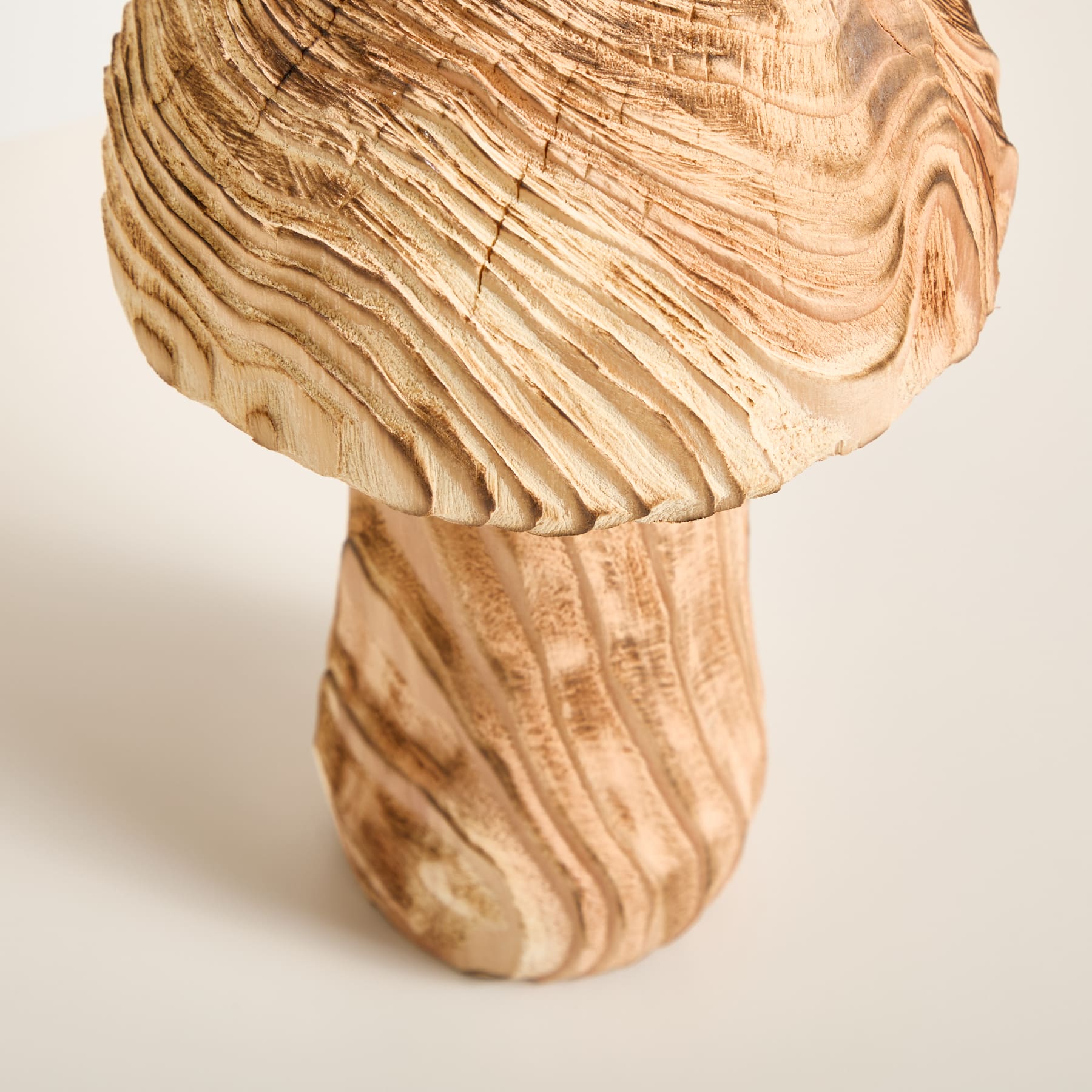 Eine pilzförmige Holzskulptur mit komplizierten, wirbelnden Mustern auf der Oberfläche, vor einem schlichten, hellen Hintergrund.