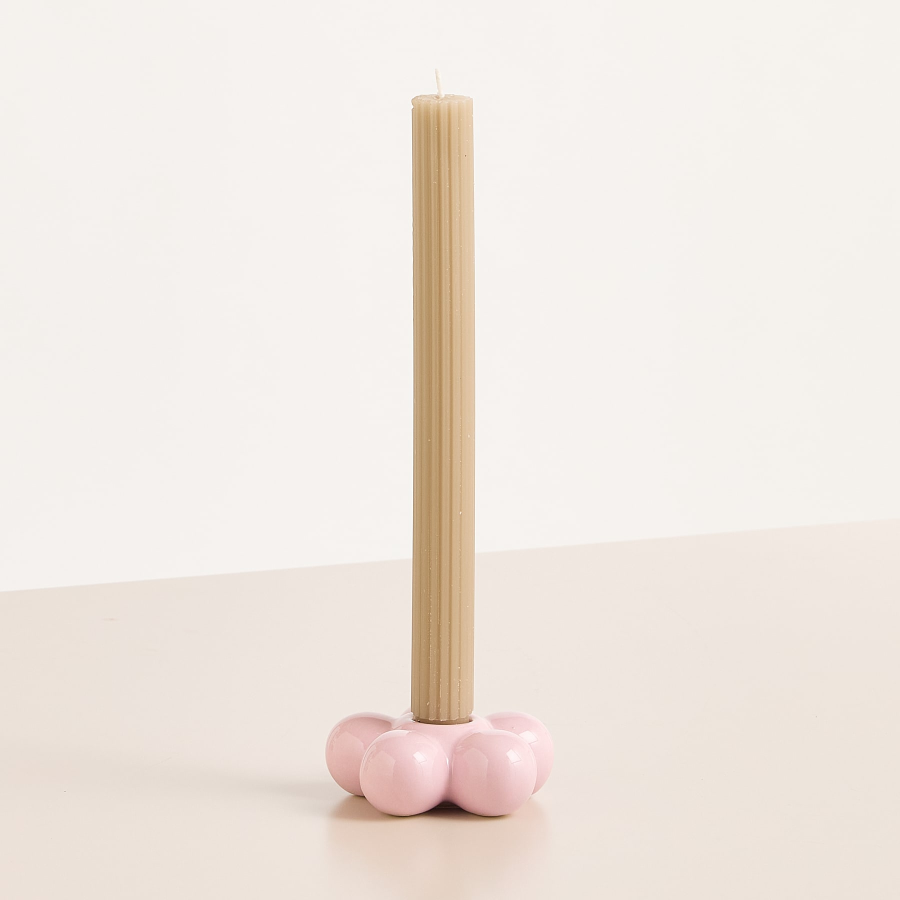 Ein Holzdübel steht aufrecht und ruht auf einer Gruppe rosafarbener, kugelförmiger Objekte vor einem schlichten weißen Hintergrund.