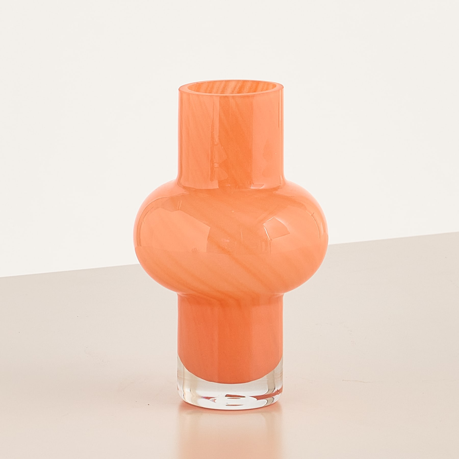 Eine leuchtend orangefarbene Glasvase mit einer einzigartigen, geometrischen Form steht auf einer schlichten, hellen Oberfläche.